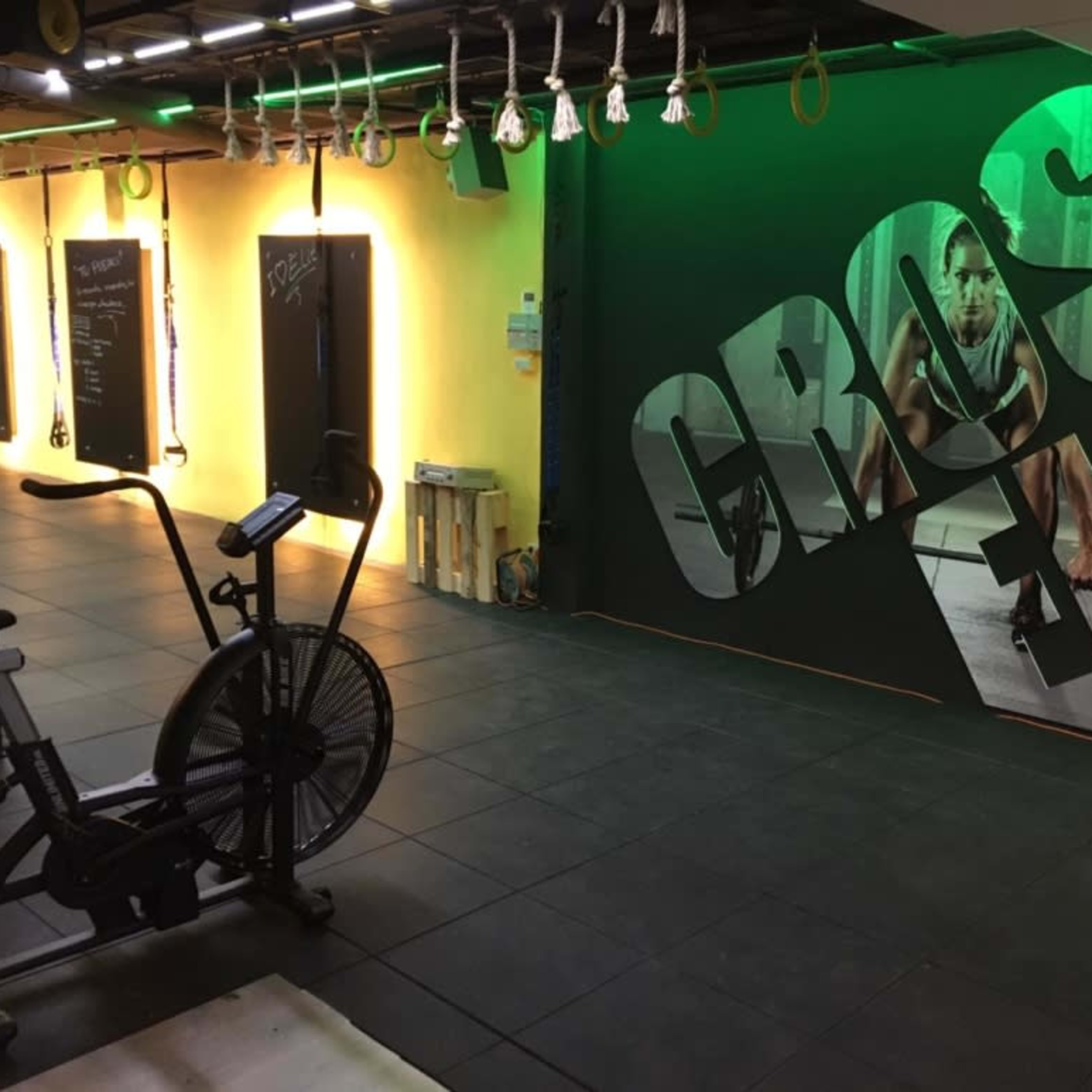 A fitness studio with an exercise bike in the foreground and a large wall mural of a person working out in the background, illuminated by green and yellow lighting.
