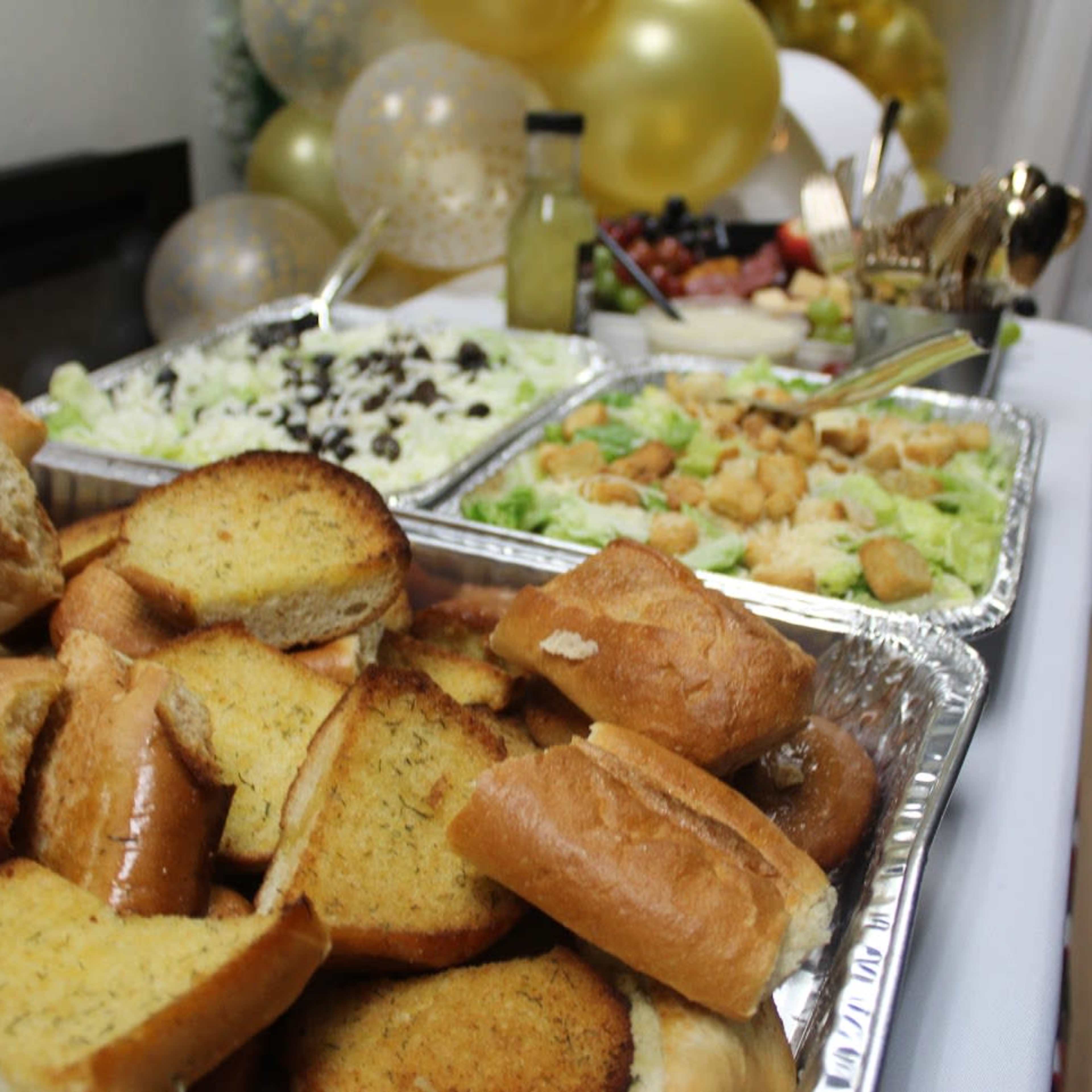 A table spread with trays of salad and garlic bread, surrounded by decorative balloons.
