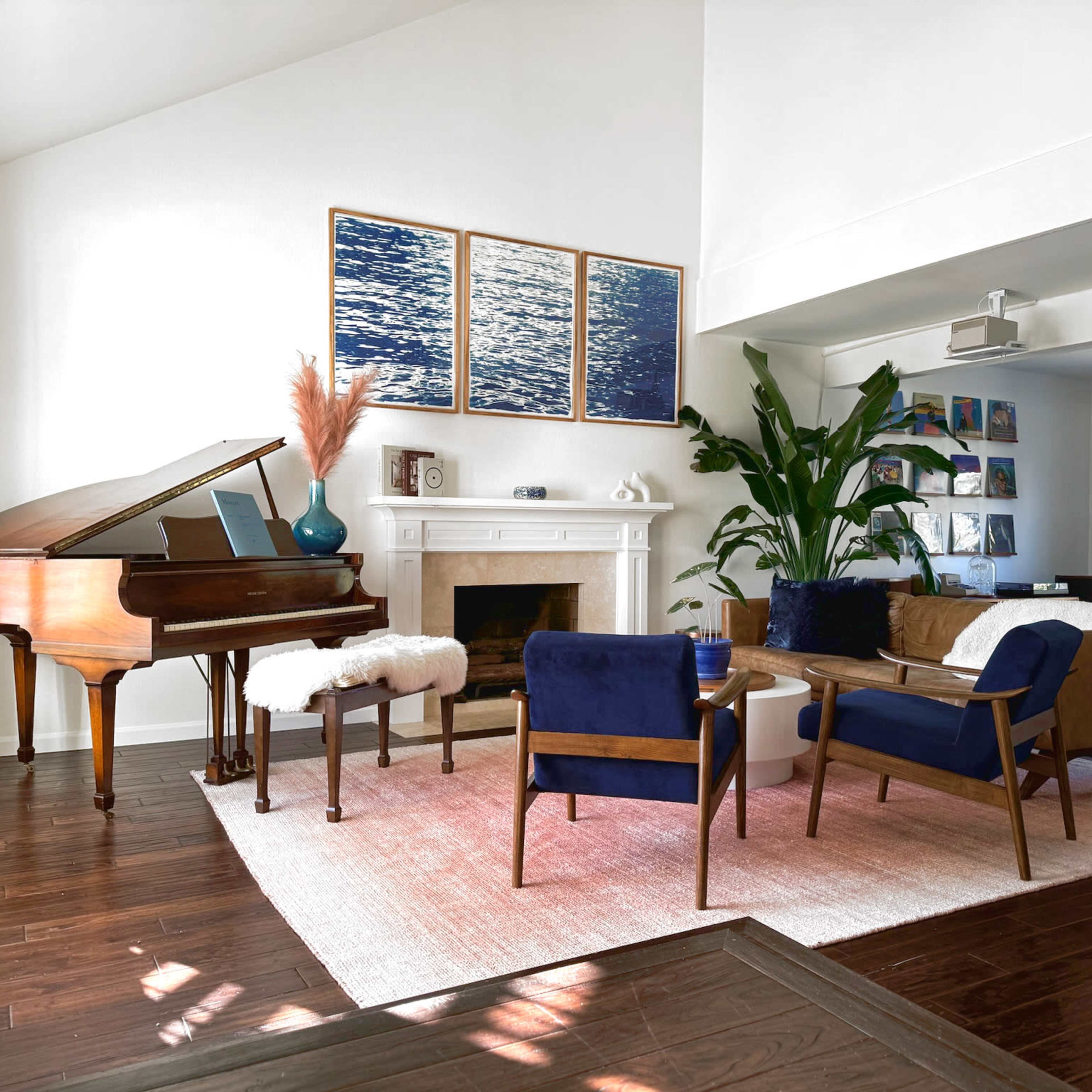 A modern living room features a grand piano, a fireplace with a white mantel, and a mix of comfortable seating around a central area rug.