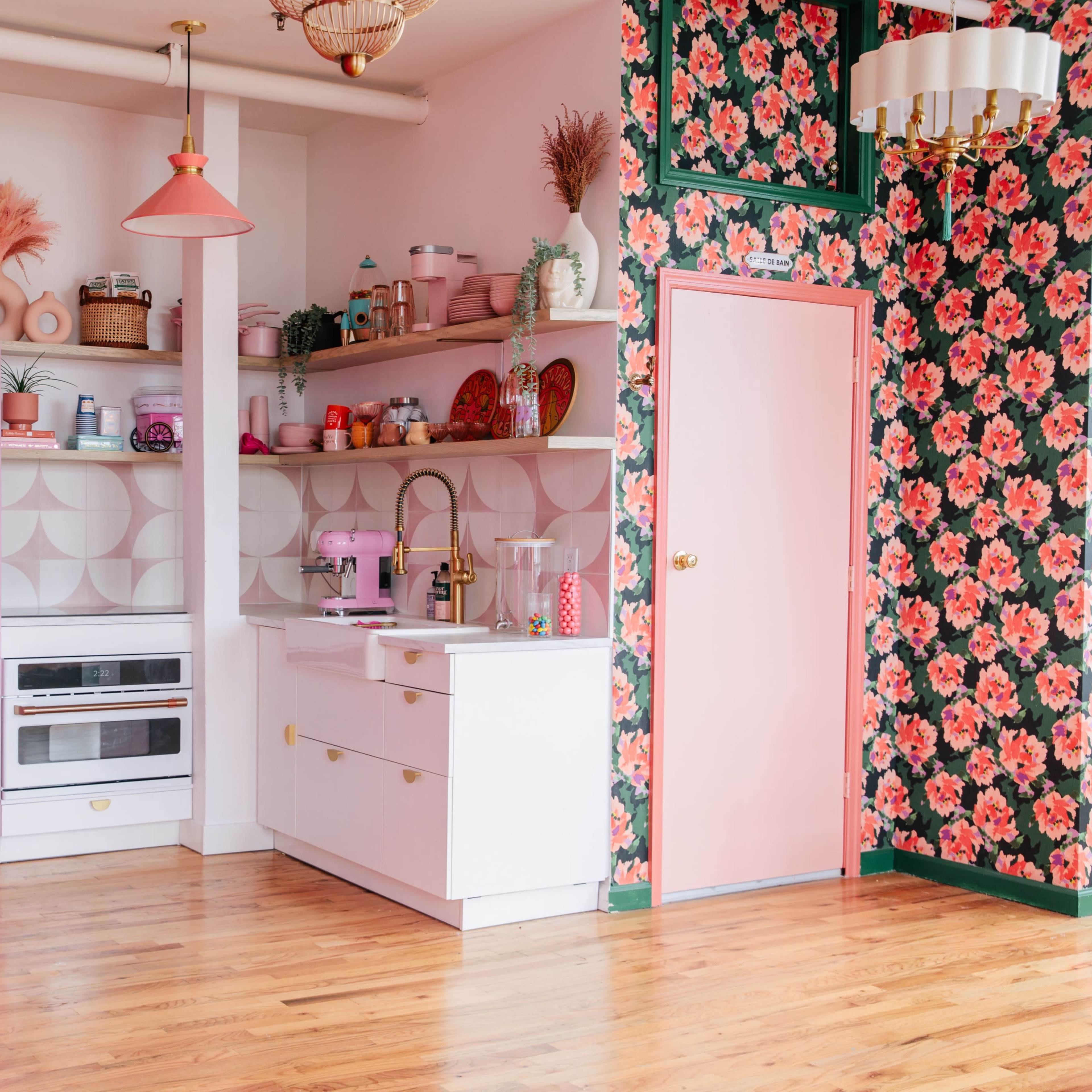 A brightly colored kitchen with pink appliances, floral wallpaper, and wooden flooring.