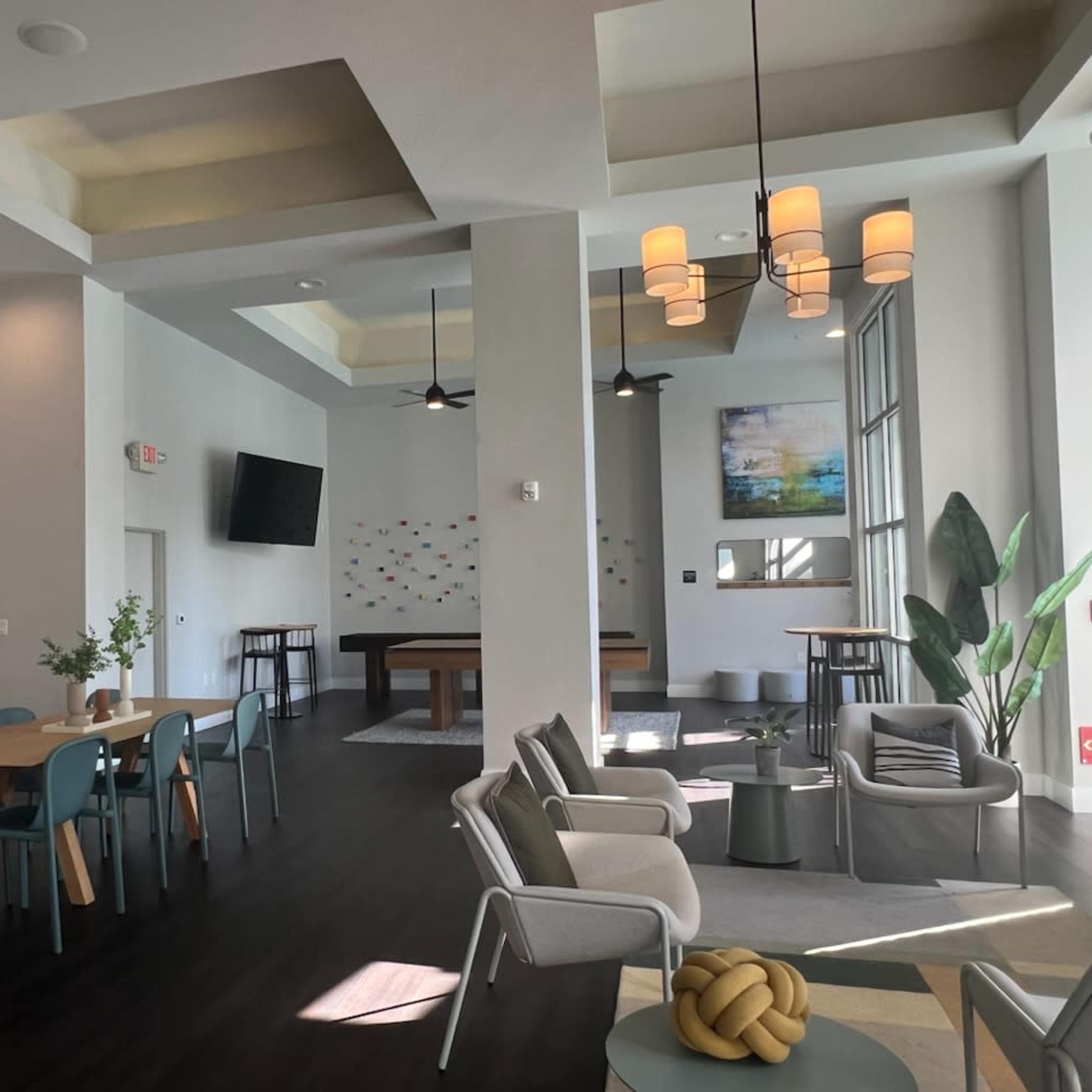 A modern lounge area featuring a seating arrangement with chairs and a table, a pool table, and large windows allowing natural light to enter.