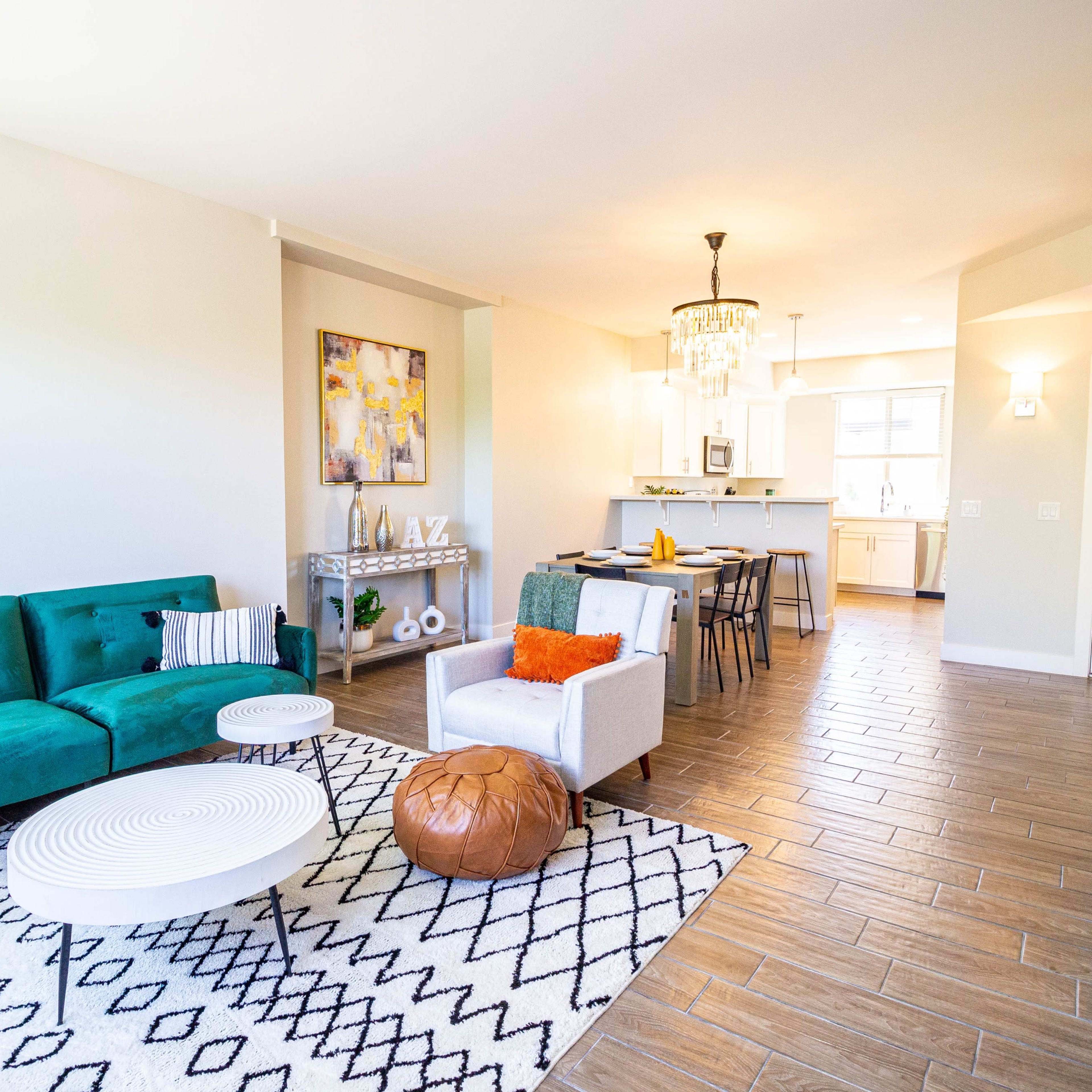 A spacious living area features a green couch, a white coffee table, and a decorative area rug, leading to a kitchen and dining space in the background.