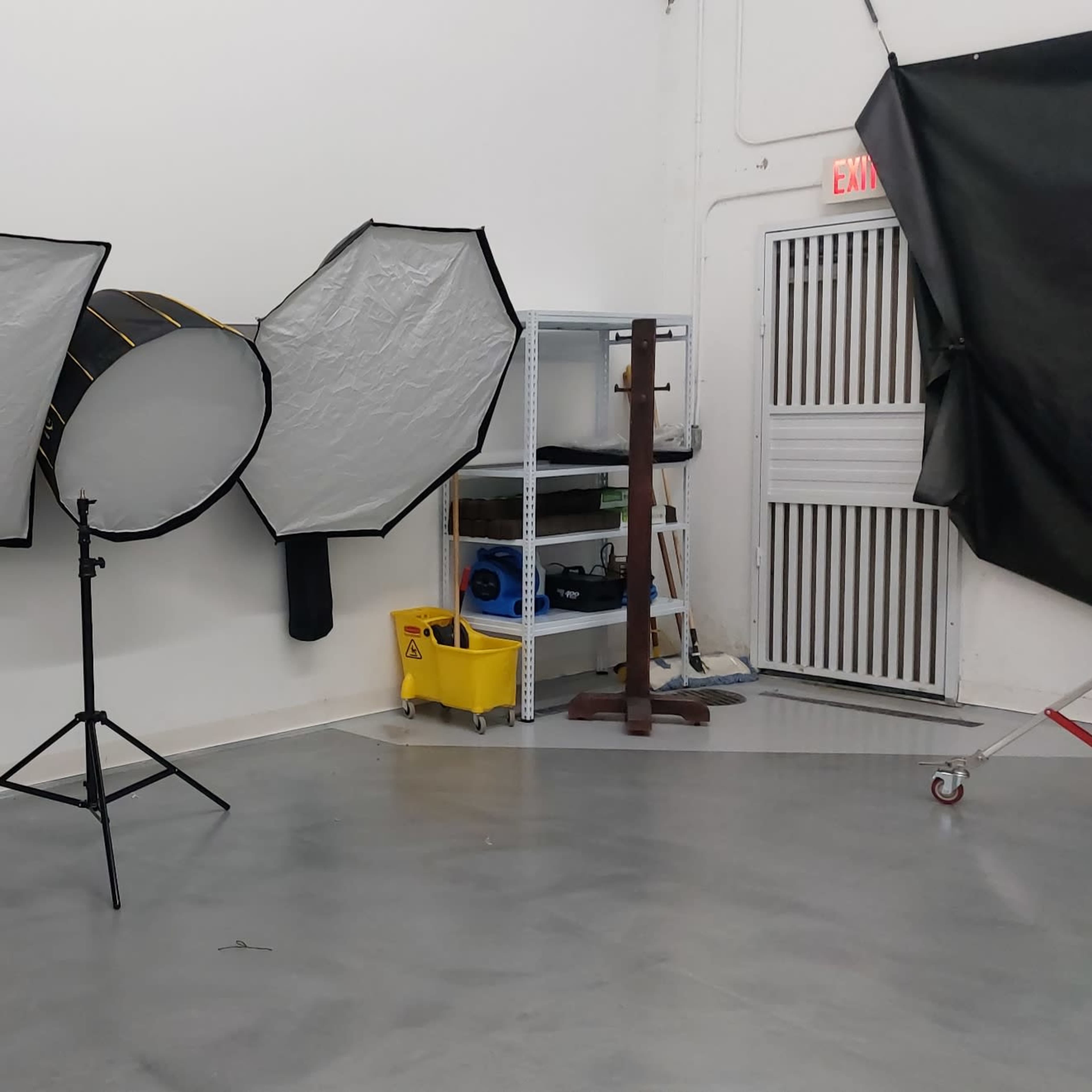 A photography studio with various lighting equipment and a shelving unit in a brightly lit room.