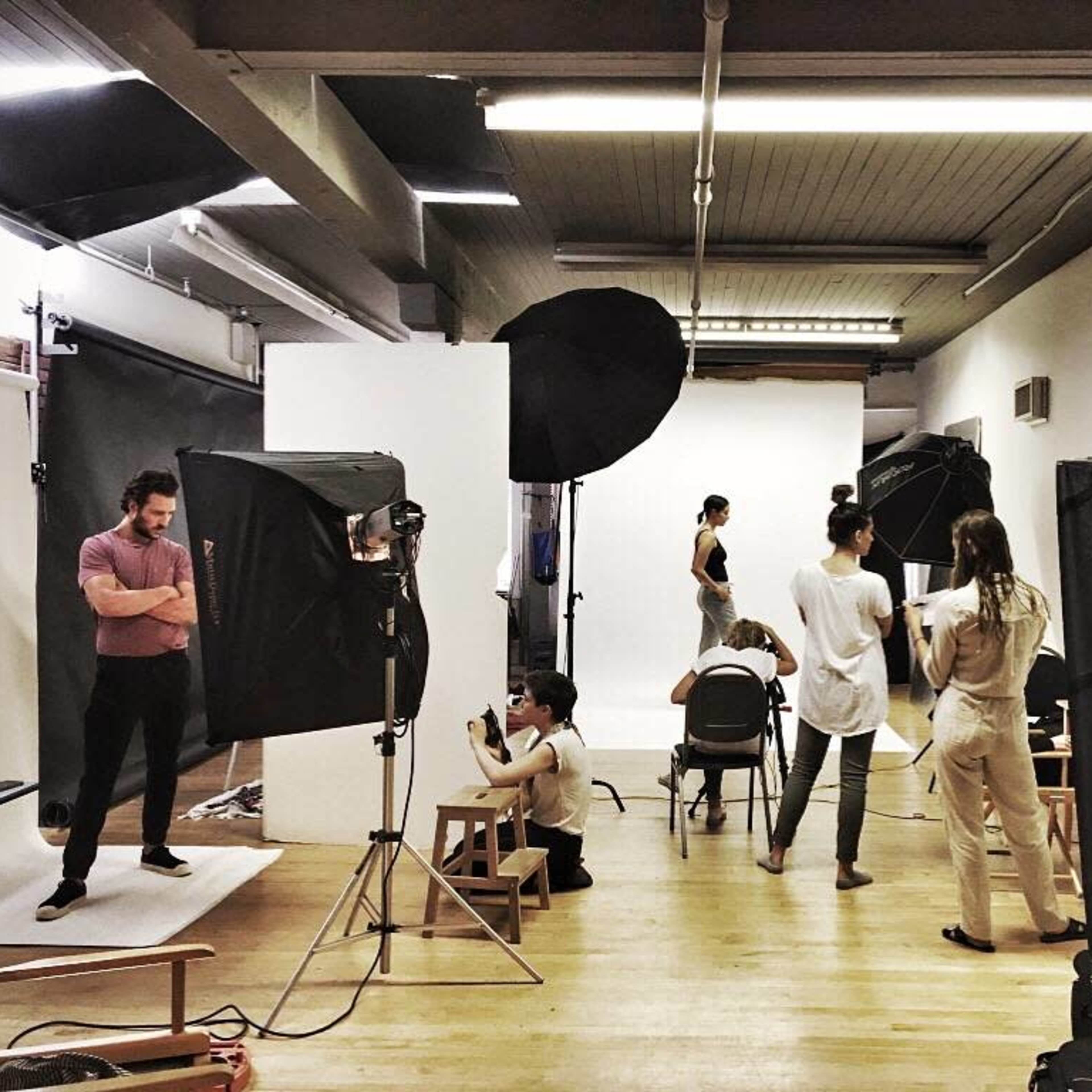 A photography studio is set up with several models being photographed and assistants managing lighting equipment and backgrounds.