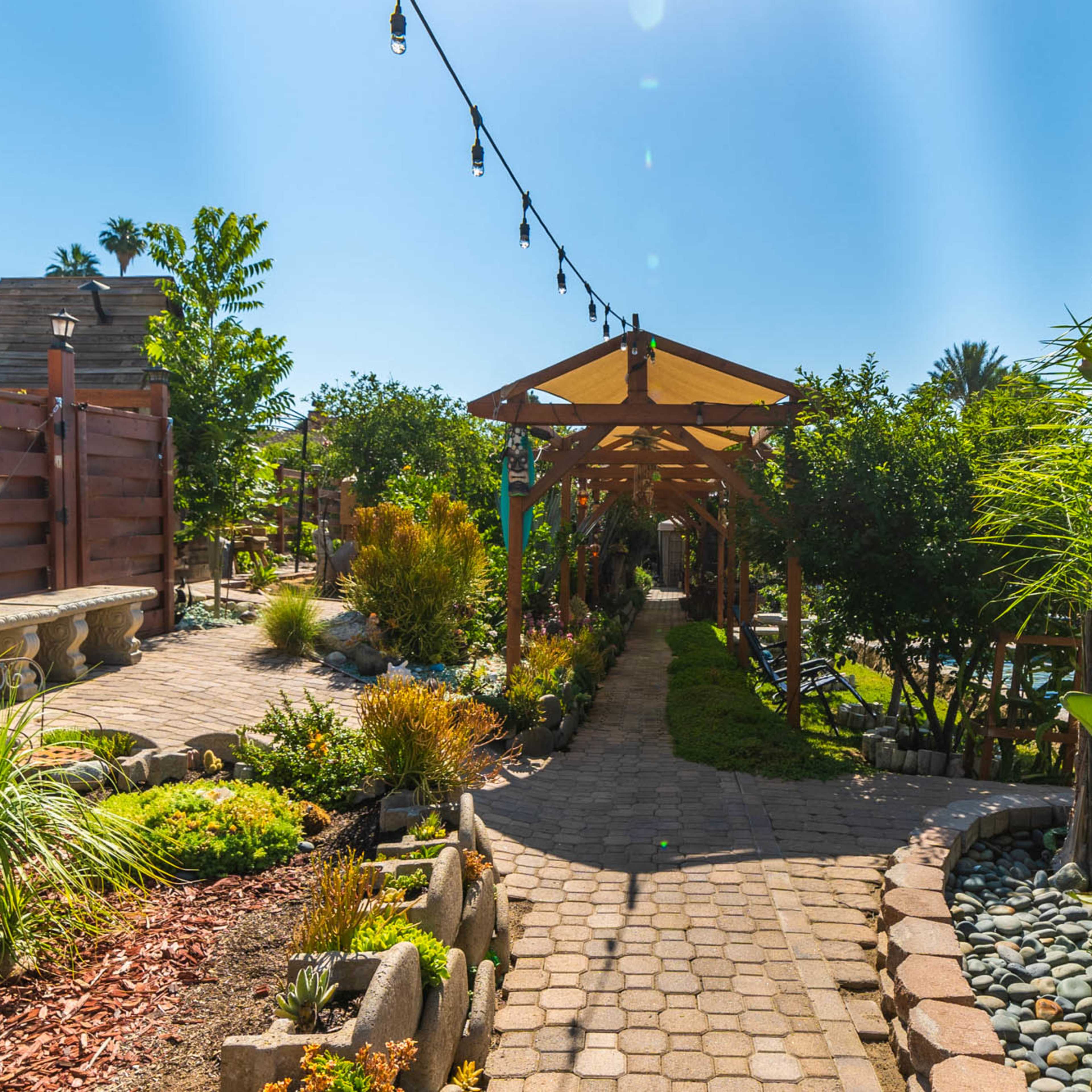 A stone pathway leads through a landscaped garden with greenery and decorative lighting overhead.