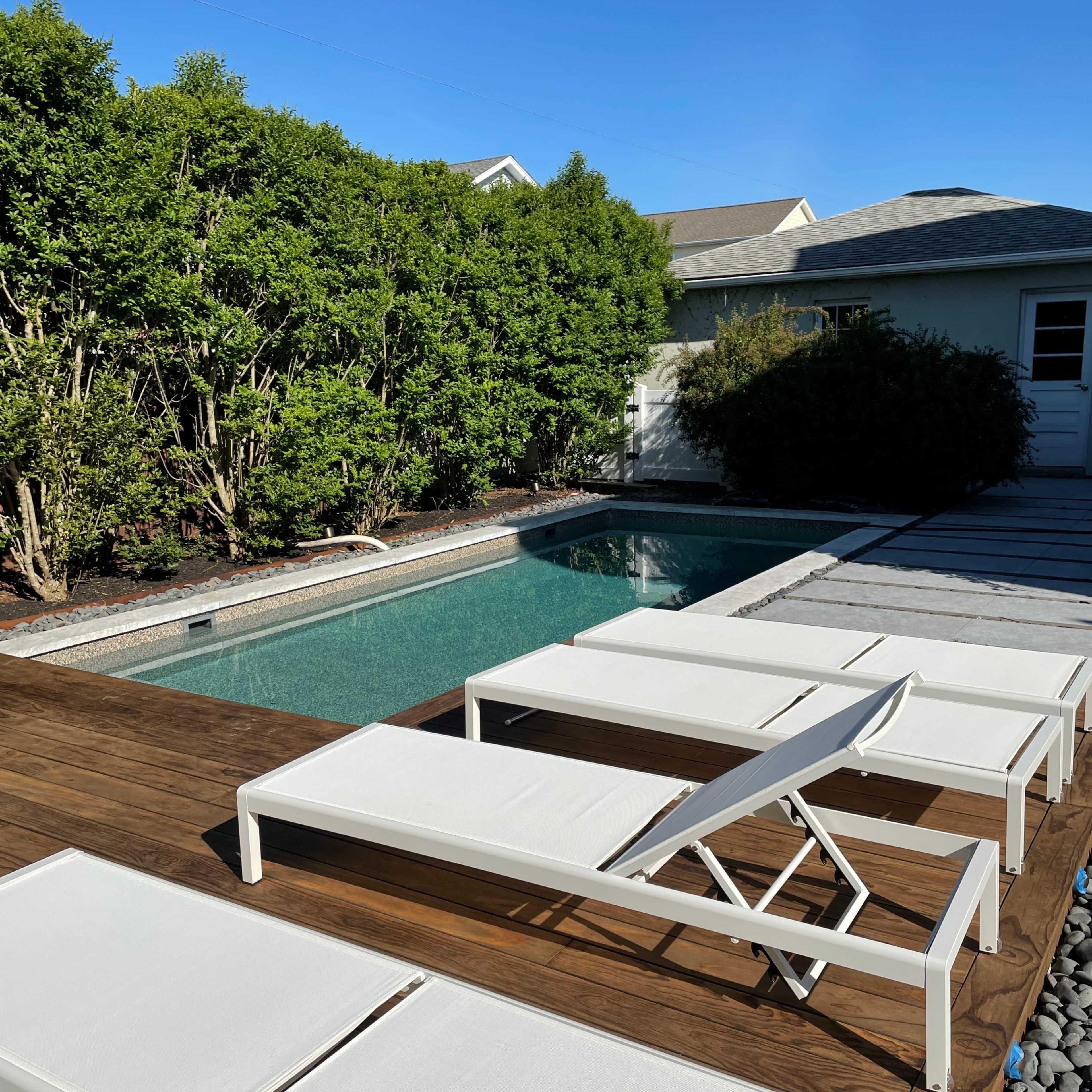 A backyard with a swimming pool surrounded by wooden decking and white lounge chairs.