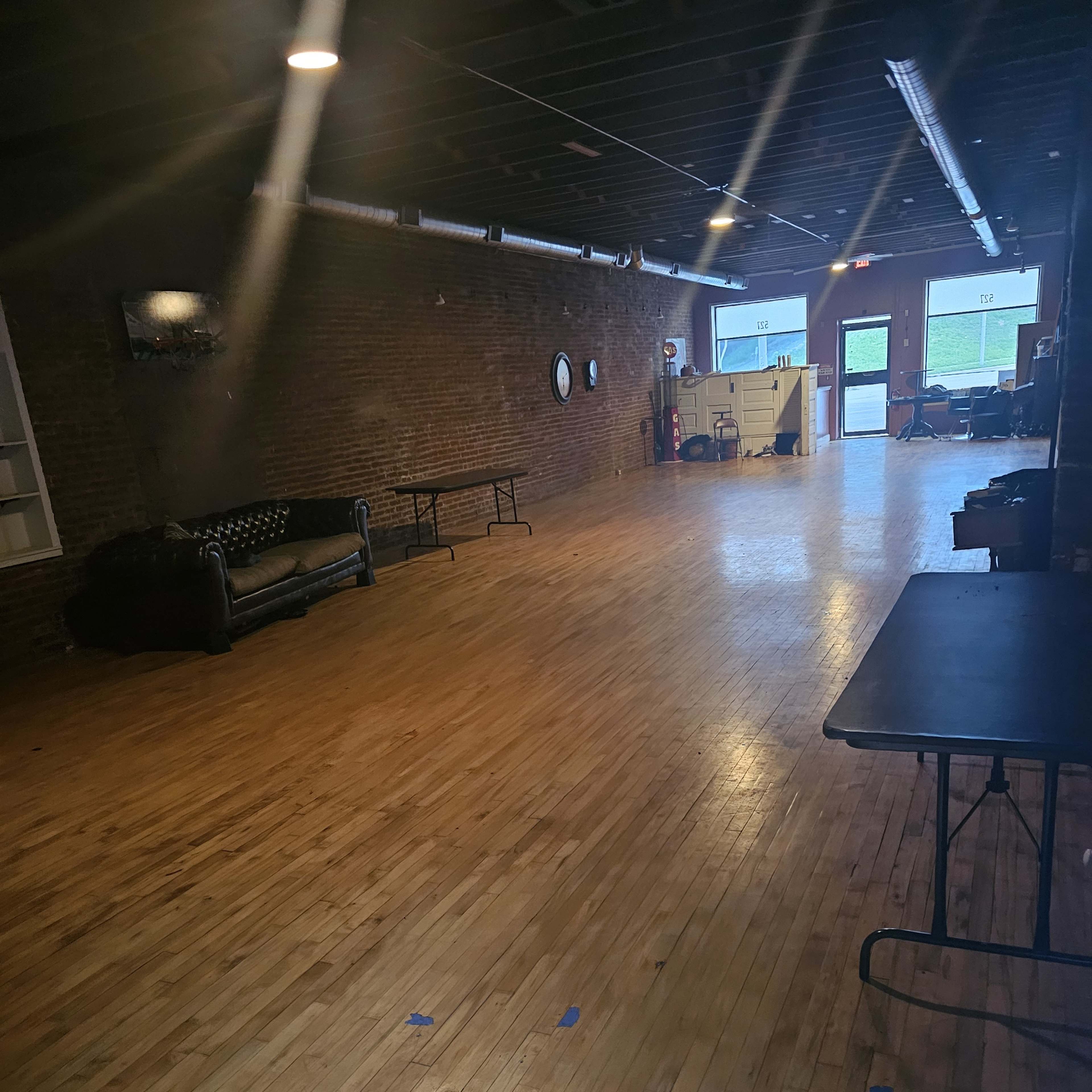 An empty room with wooden flooring, exposed brick walls, and a few pieces of furniture, including a couch and tables.