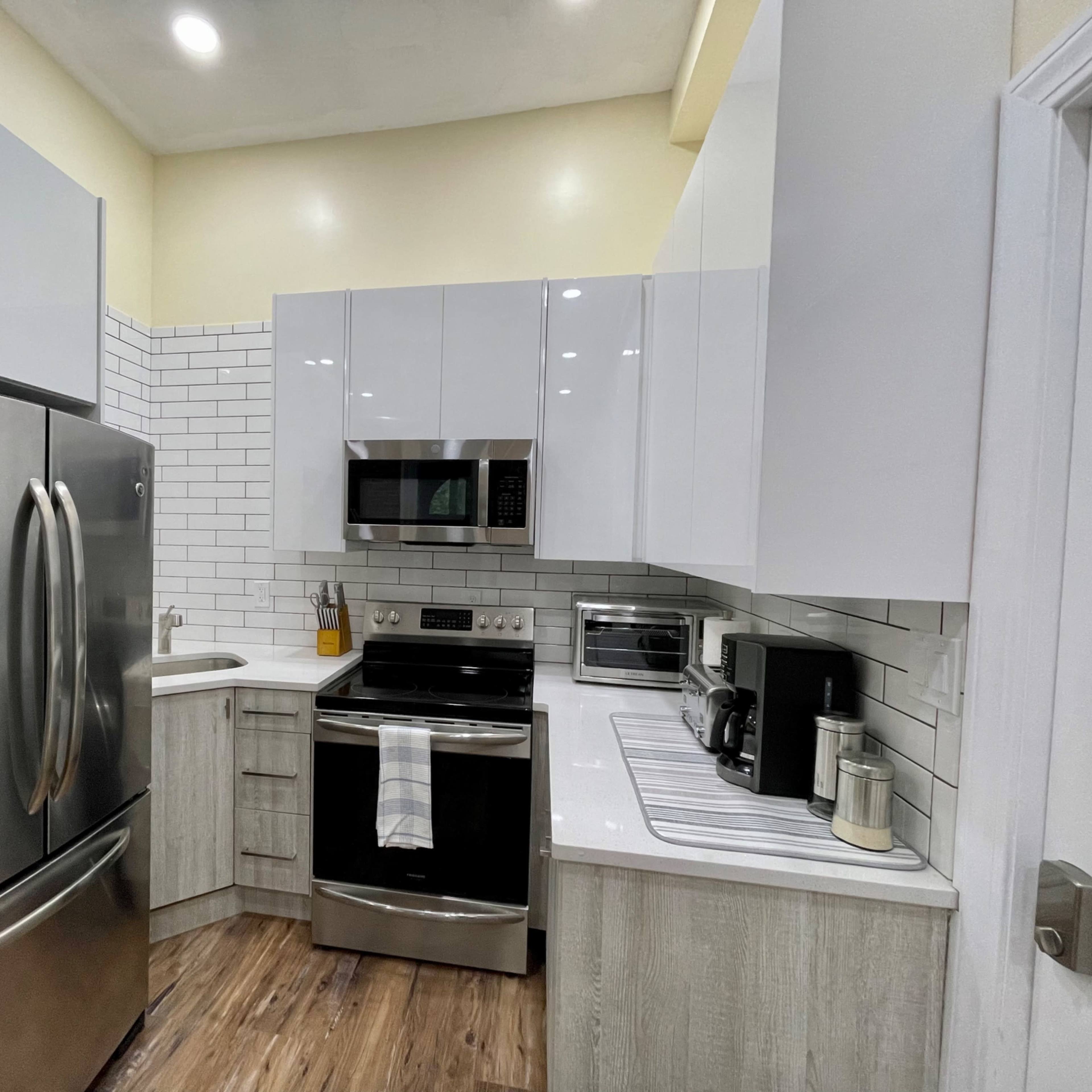 A modern kitchen with stainless steel appliances, white cabinetry, and a combination of tiled and wooden flooring.