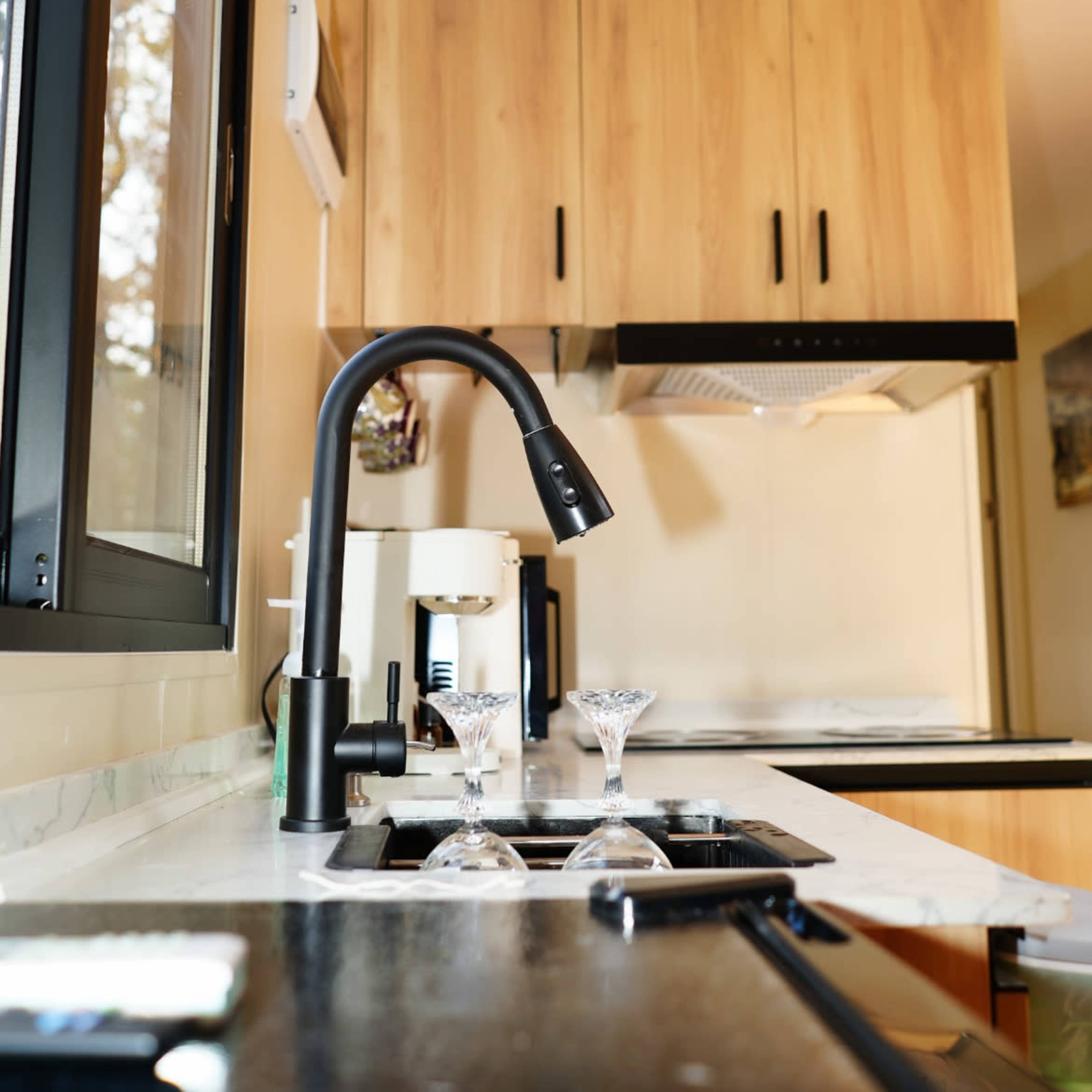 A modern kitchen with a black faucet, a coffee maker, and two crystal glasses on a marble countertop.