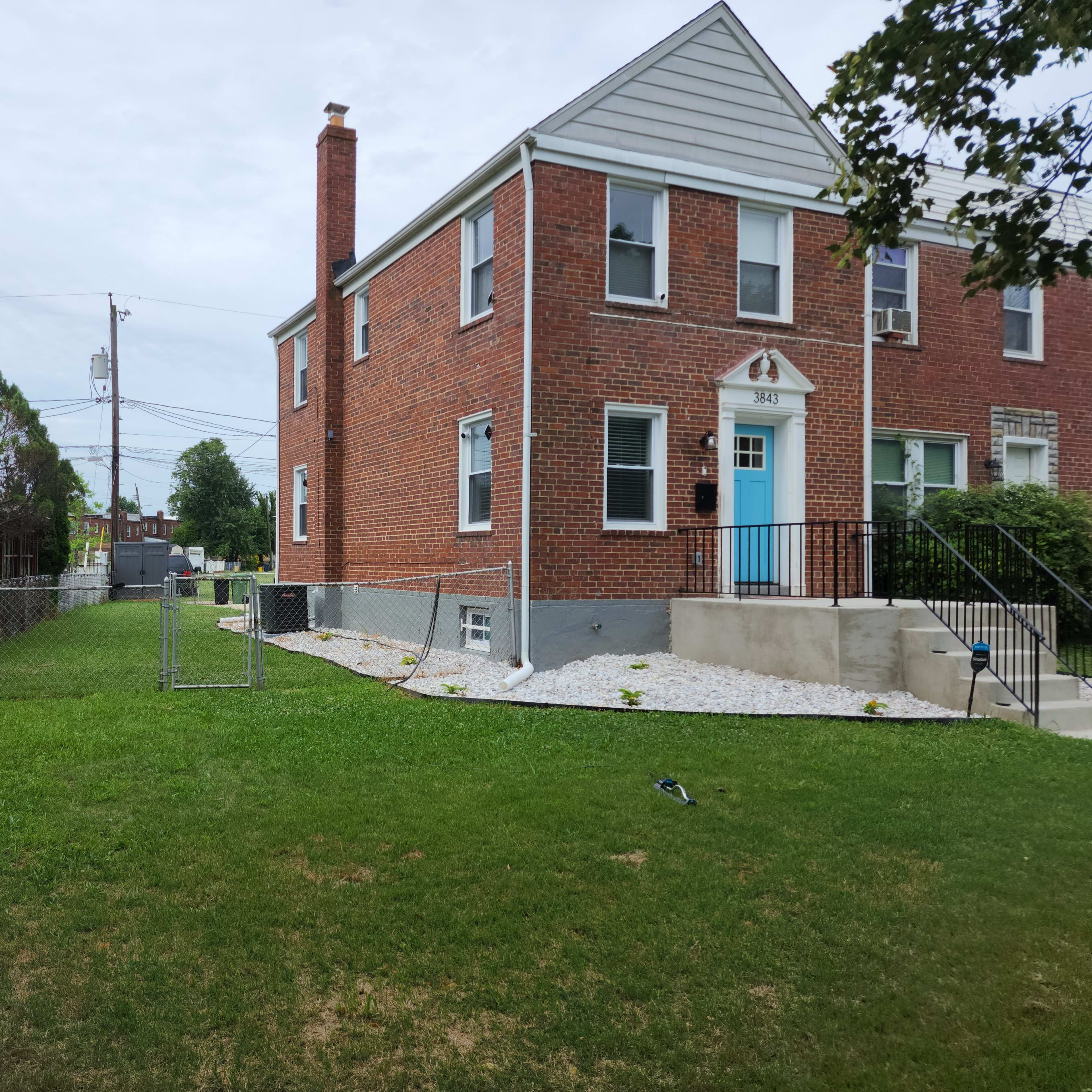 A two-story brick house with a light blue door, a fenced yard, and a large grassy area.
