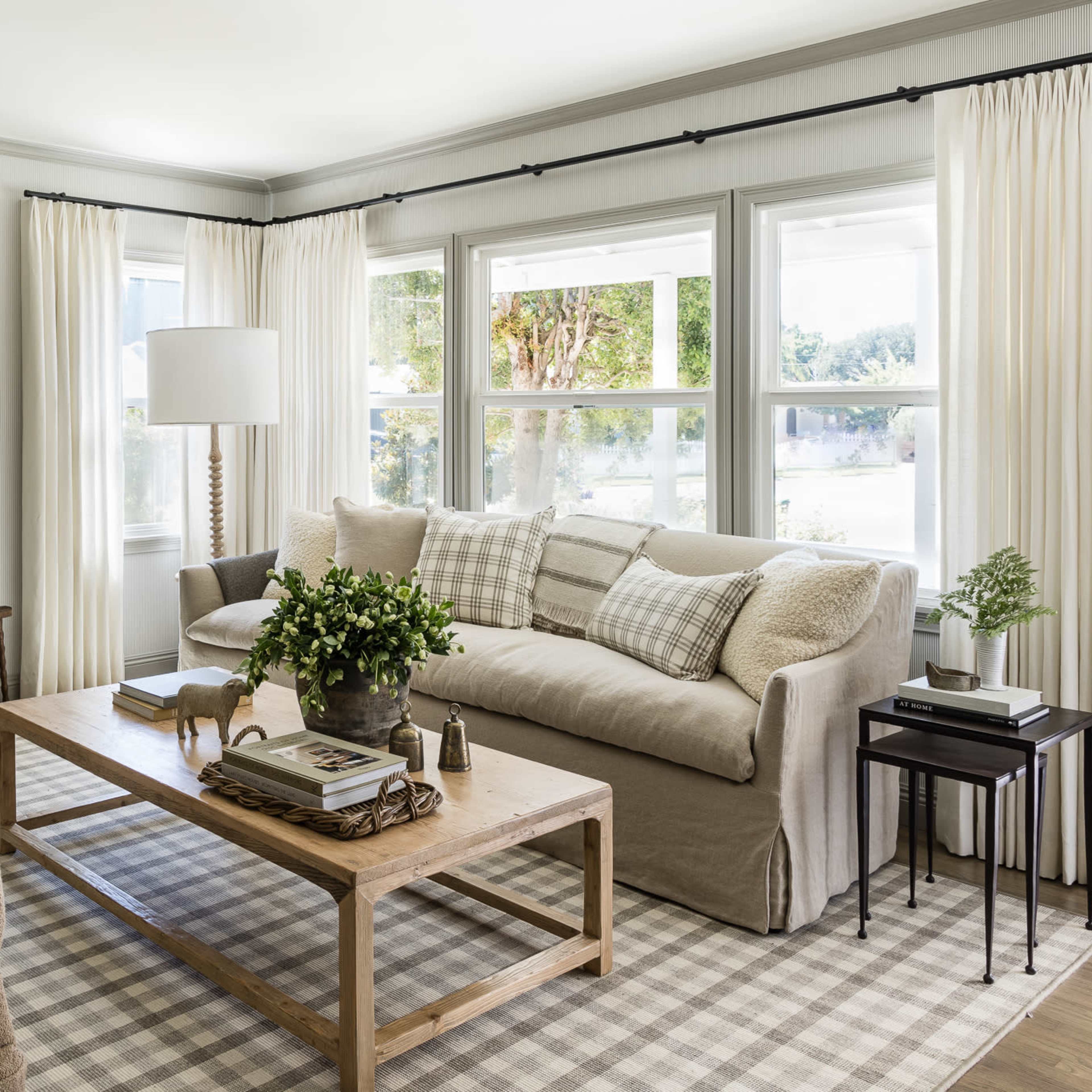 A cozy living room with a sofa, two armchairs, a coffee table, and large windows dressed with light curtains.