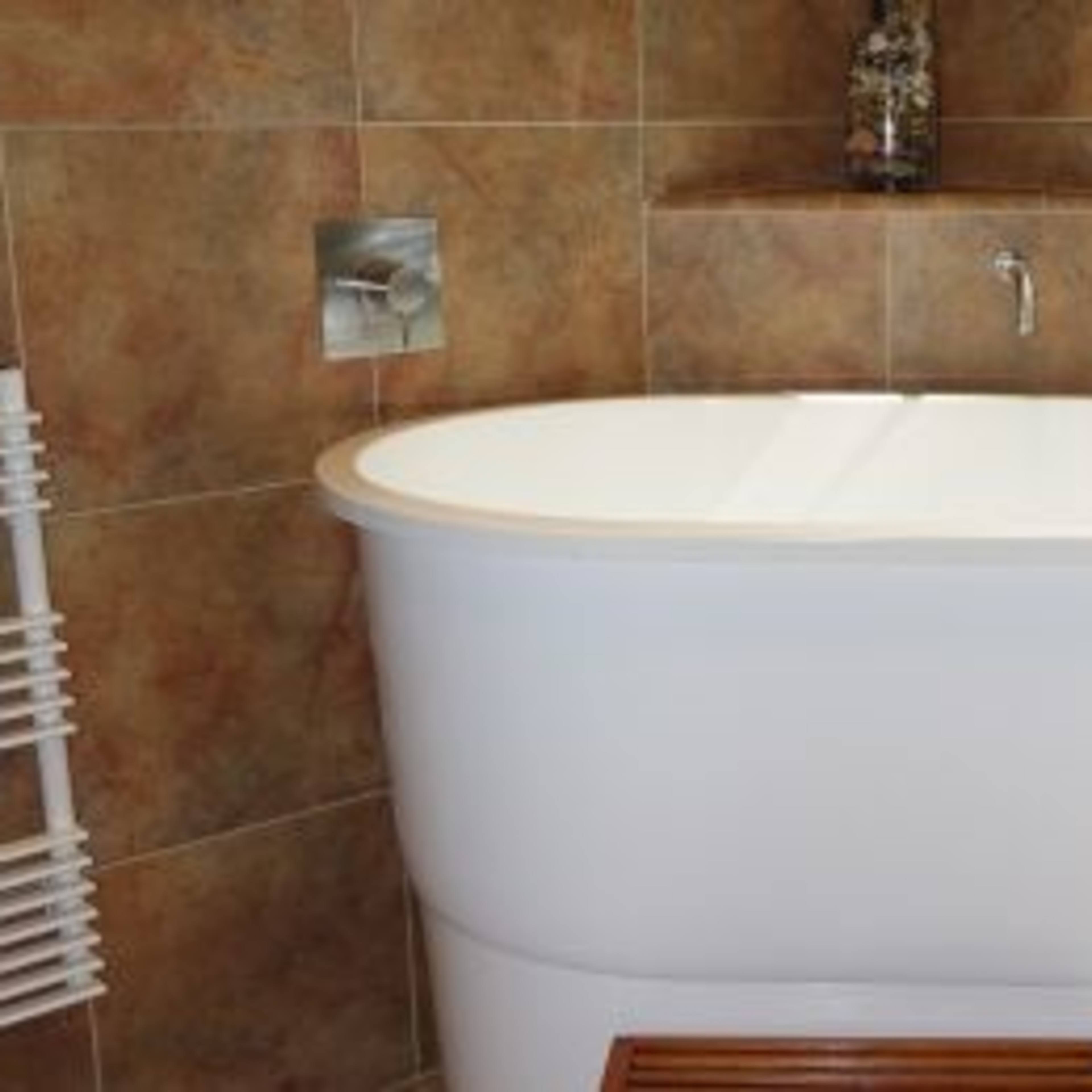 A modern, freestanding white bathtub against a tiled wall with a window overlooking greenery.