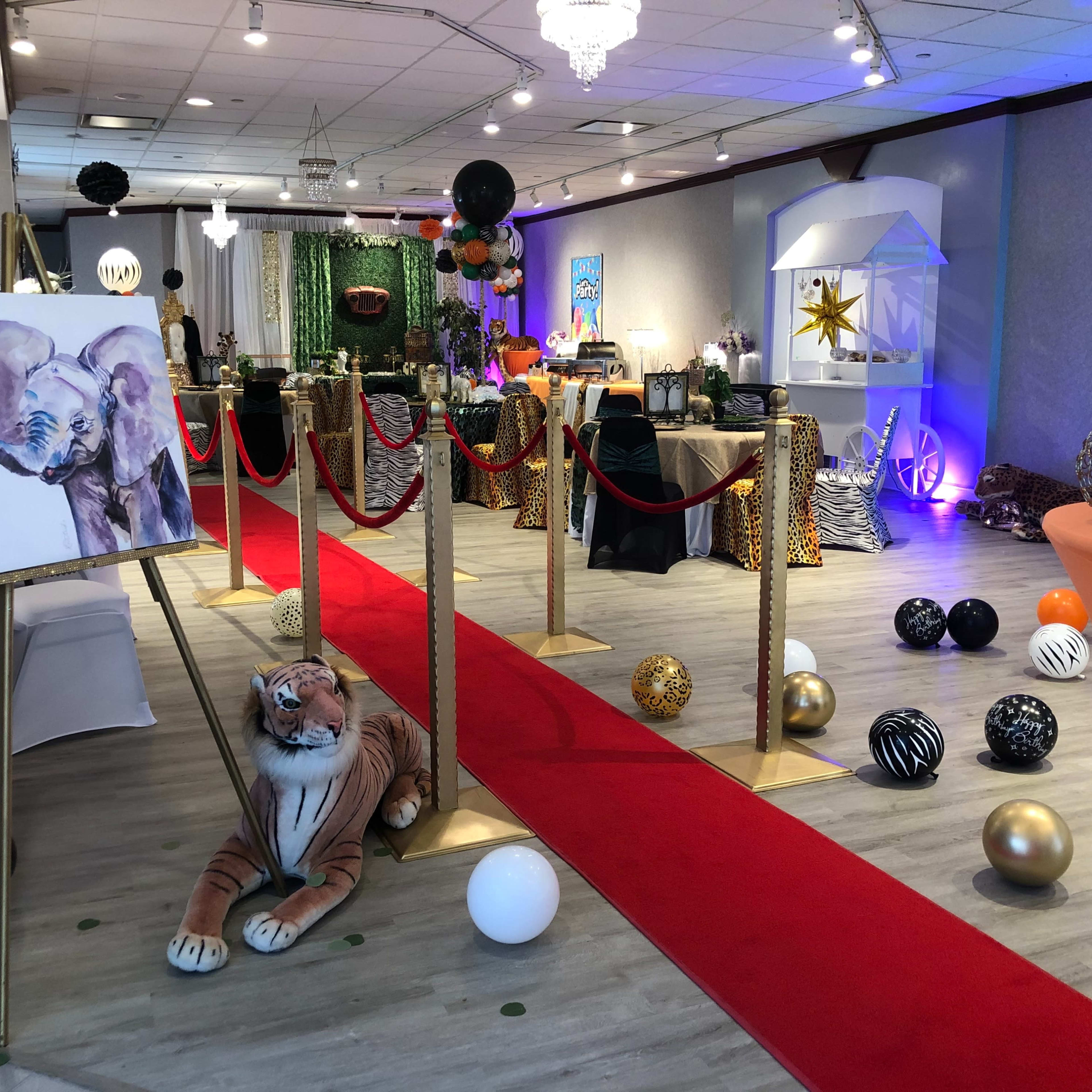 A venue is decorated with a red carpet, animal-themed decor, and an artwork of an elephant displayed on an easel.