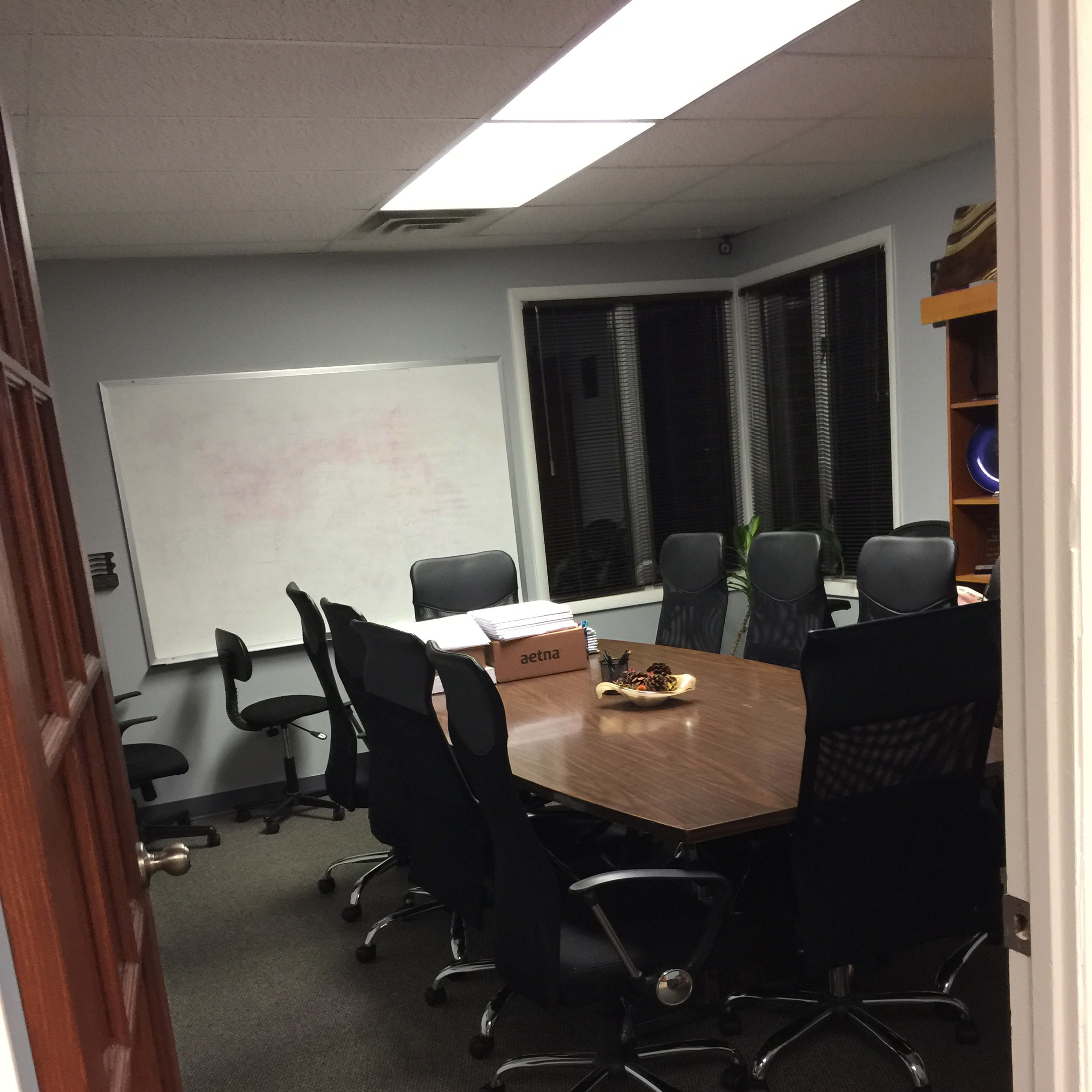 A conference room with a large table surrounded by several office chairs, a whiteboard on the wall, and a box on the table.