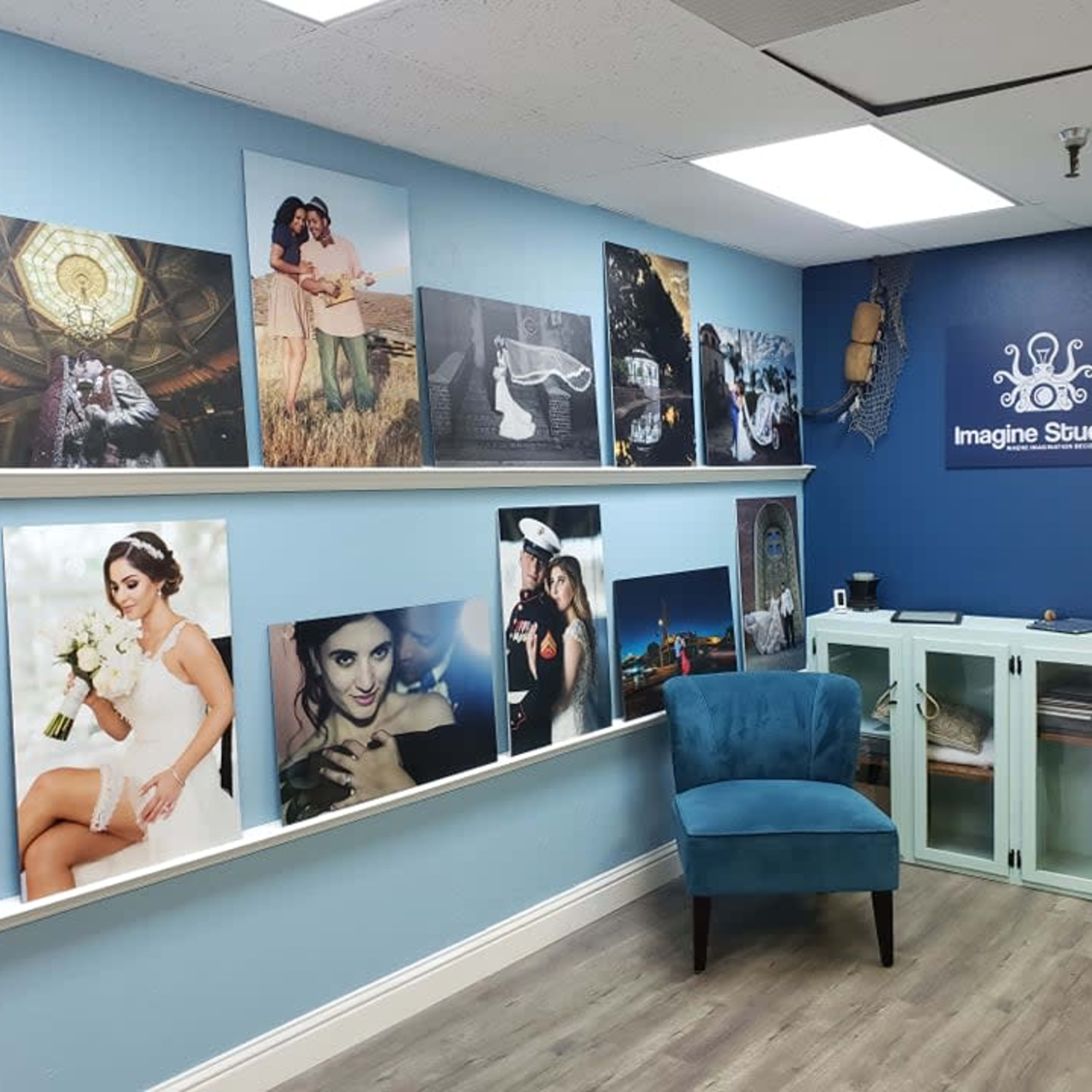 A blue-walled studio gallery featuring framed photographs, a chair, and a display cabinet.