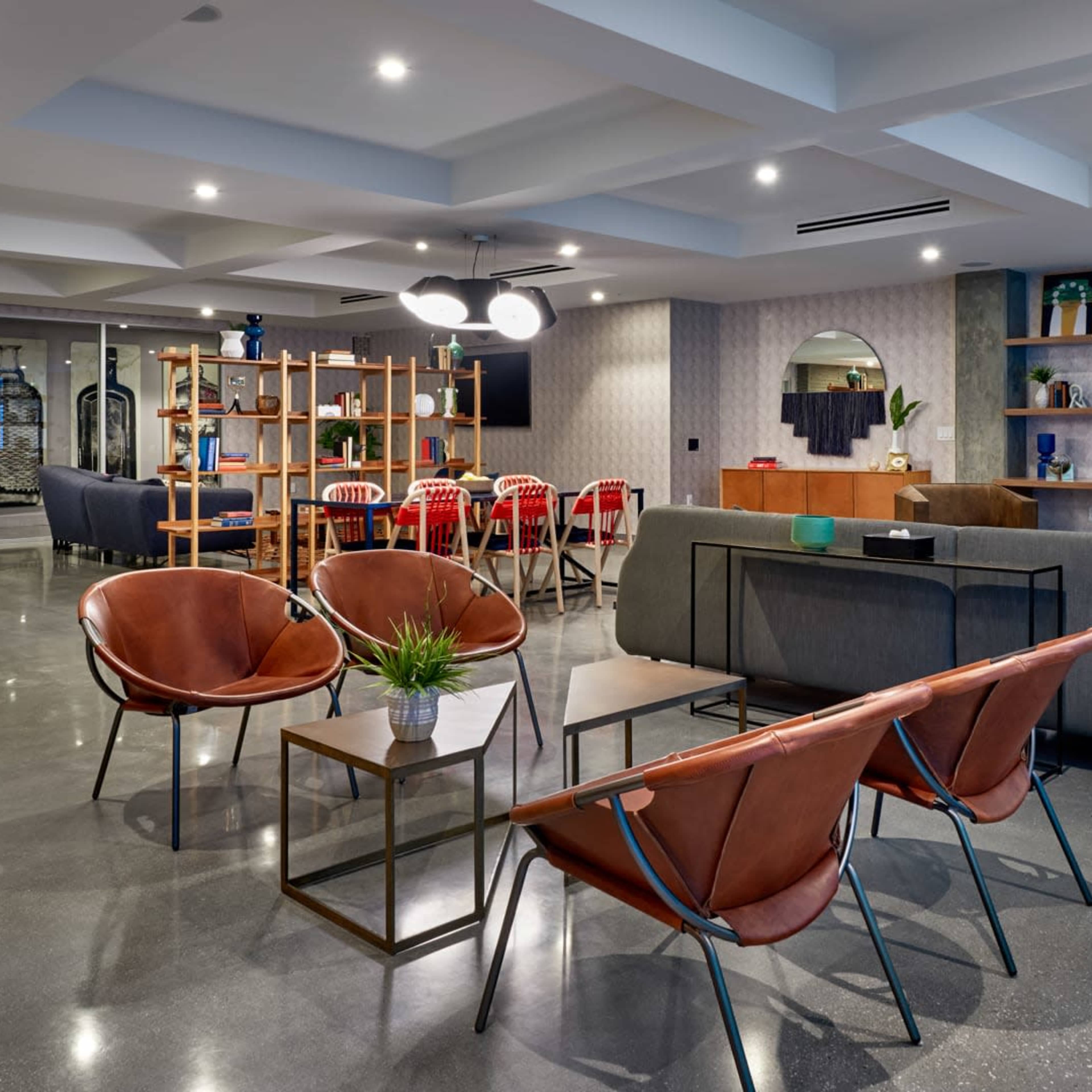 A modern communal living space with various seating arrangements, a large TV mounted on the wall, and a dining area in the background.