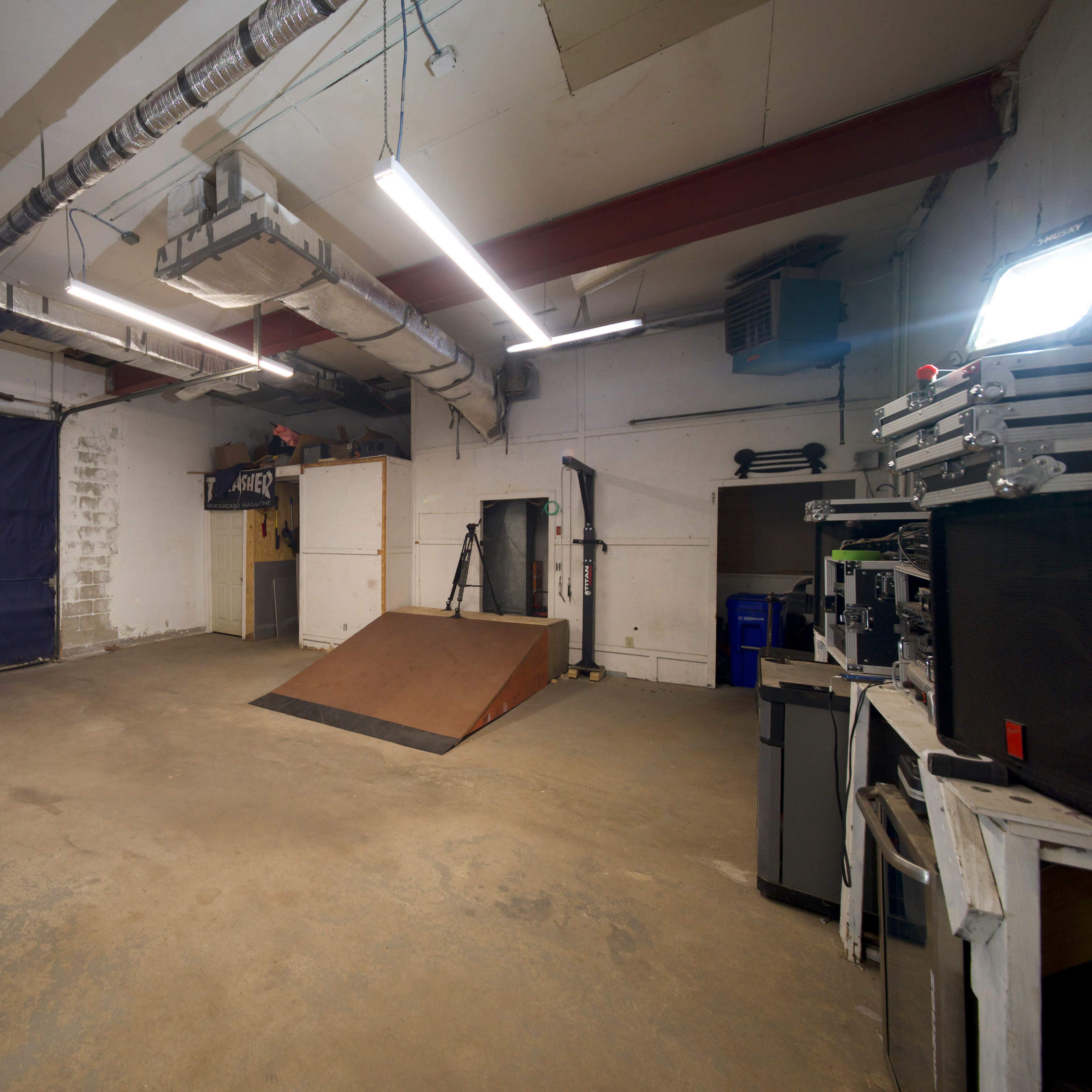 An indoor skatepark with a wooden ramp and various equipment lined up against the walls.