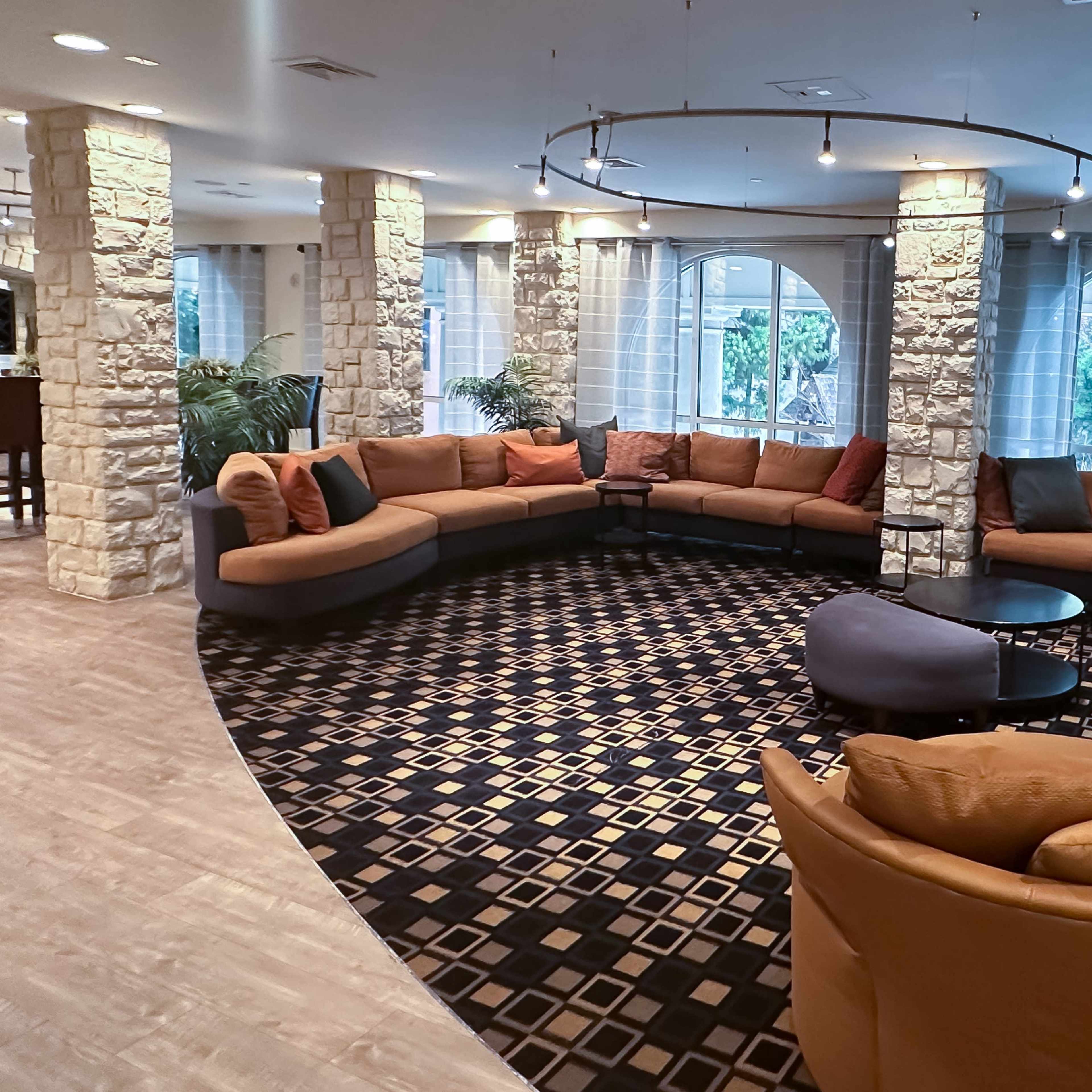 A spacious lounge area with a circular seating arrangement featuring various couches, a coffee table, and large windows overlooking greenery.