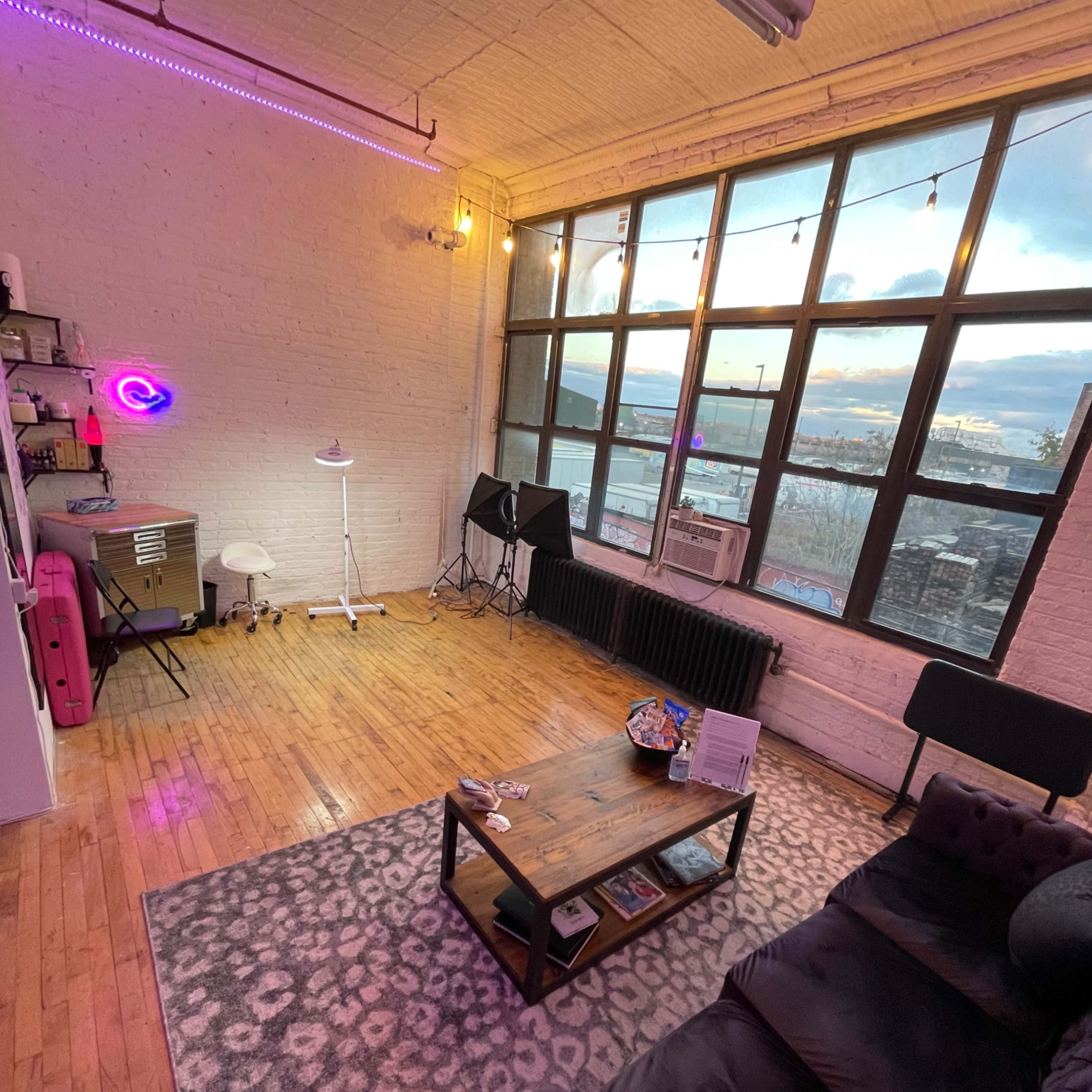A spacious room with large windows, wooden floors, and a seating area containing a sofa and a coffee table.
