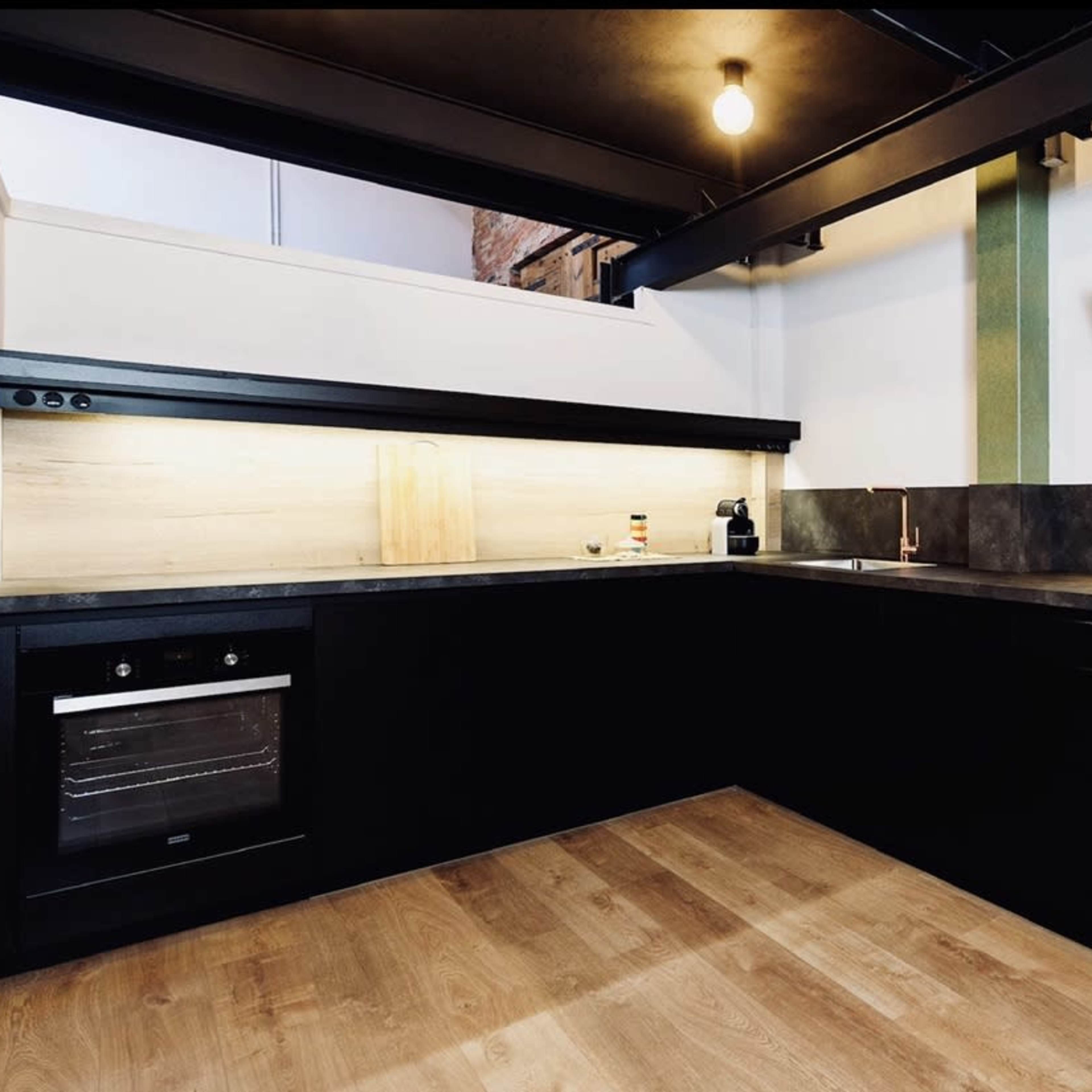 A modern kitchen with dark cabinetry, a built-in oven, and under-cabinet lighting on a light-colored wall.