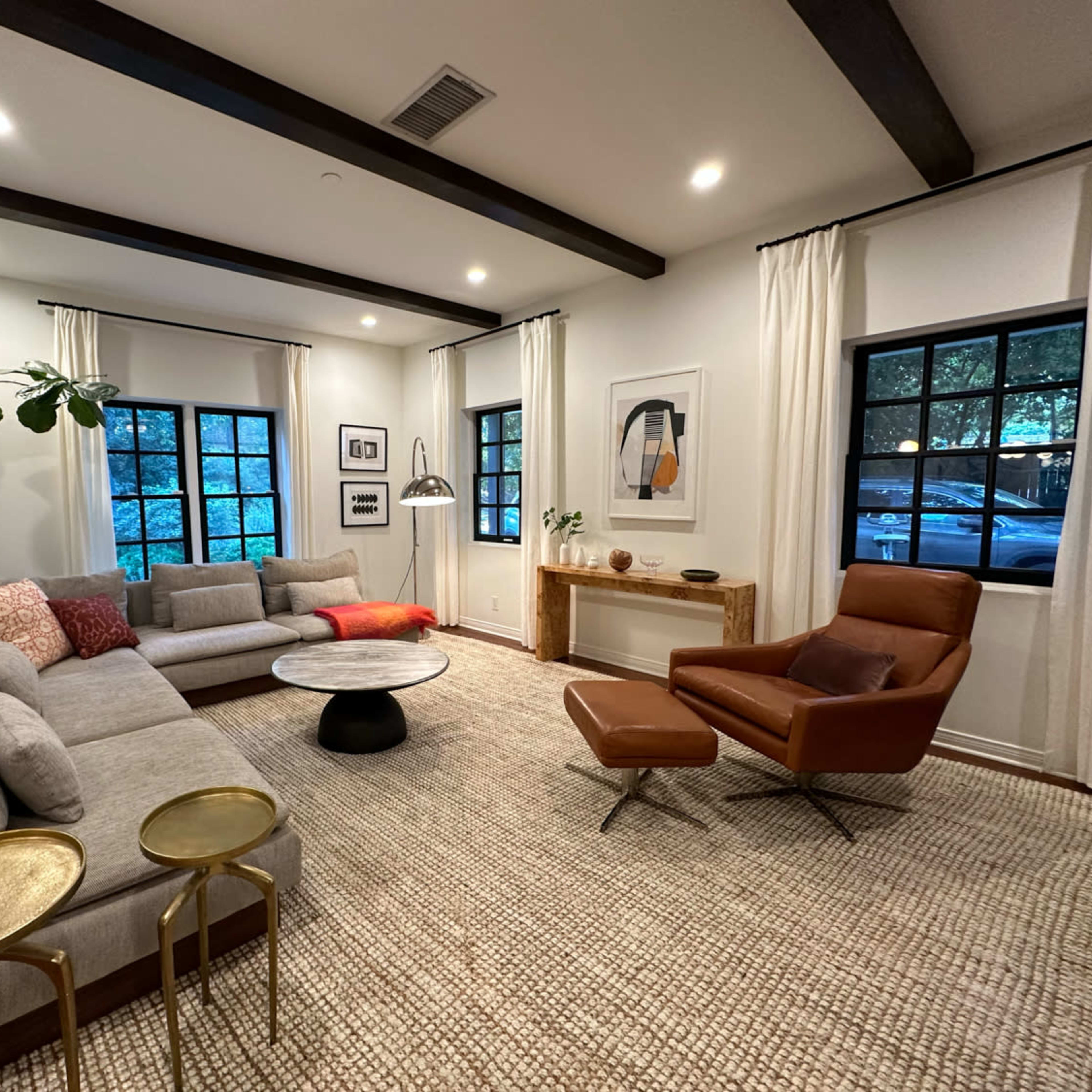 A modern living room with a large sectional sofa, an accent chair, a round coffee table, and natural light coming through two windows.