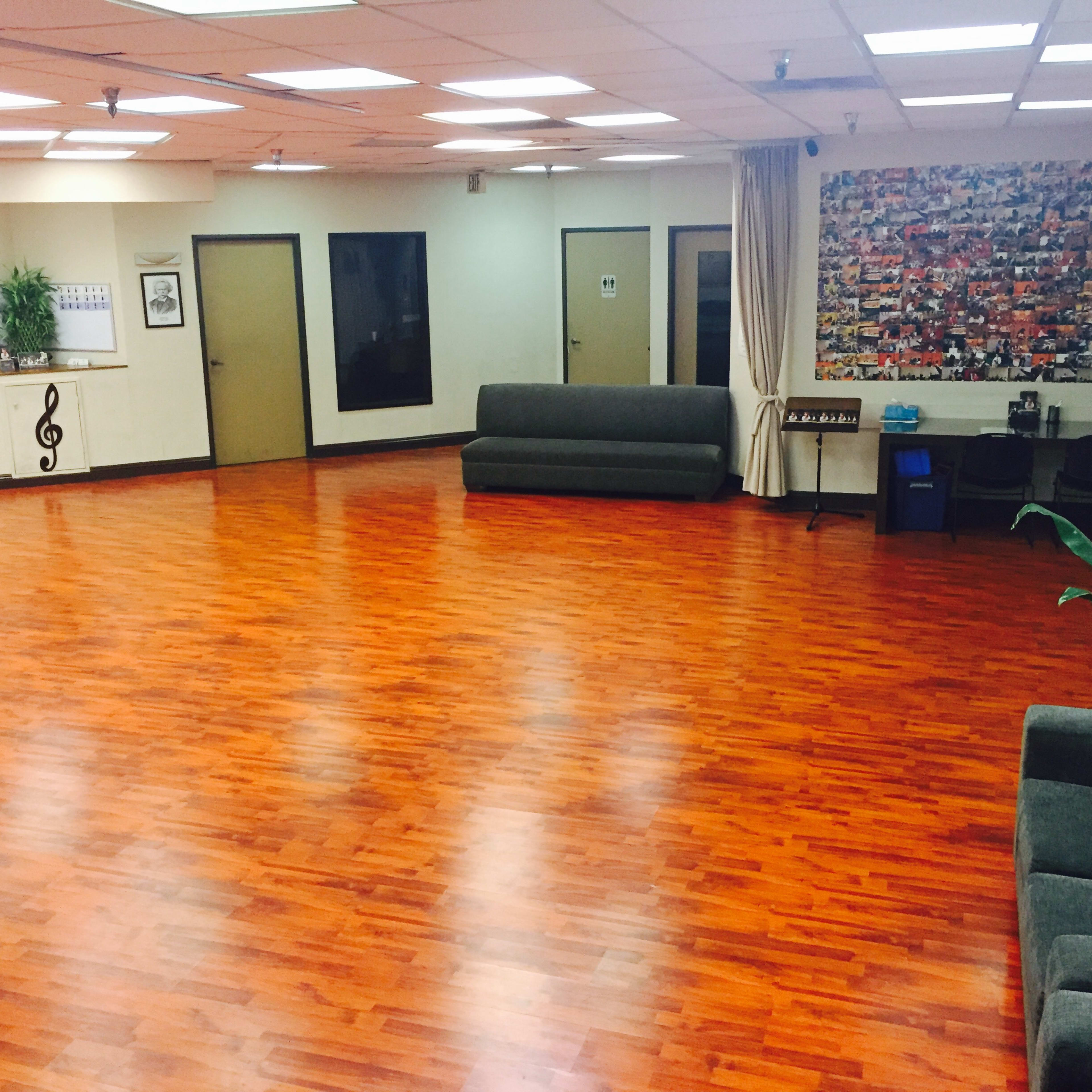 A spacious, wood-floored room with a few couches, walls adorned with framed art, and a small plant in the corner.