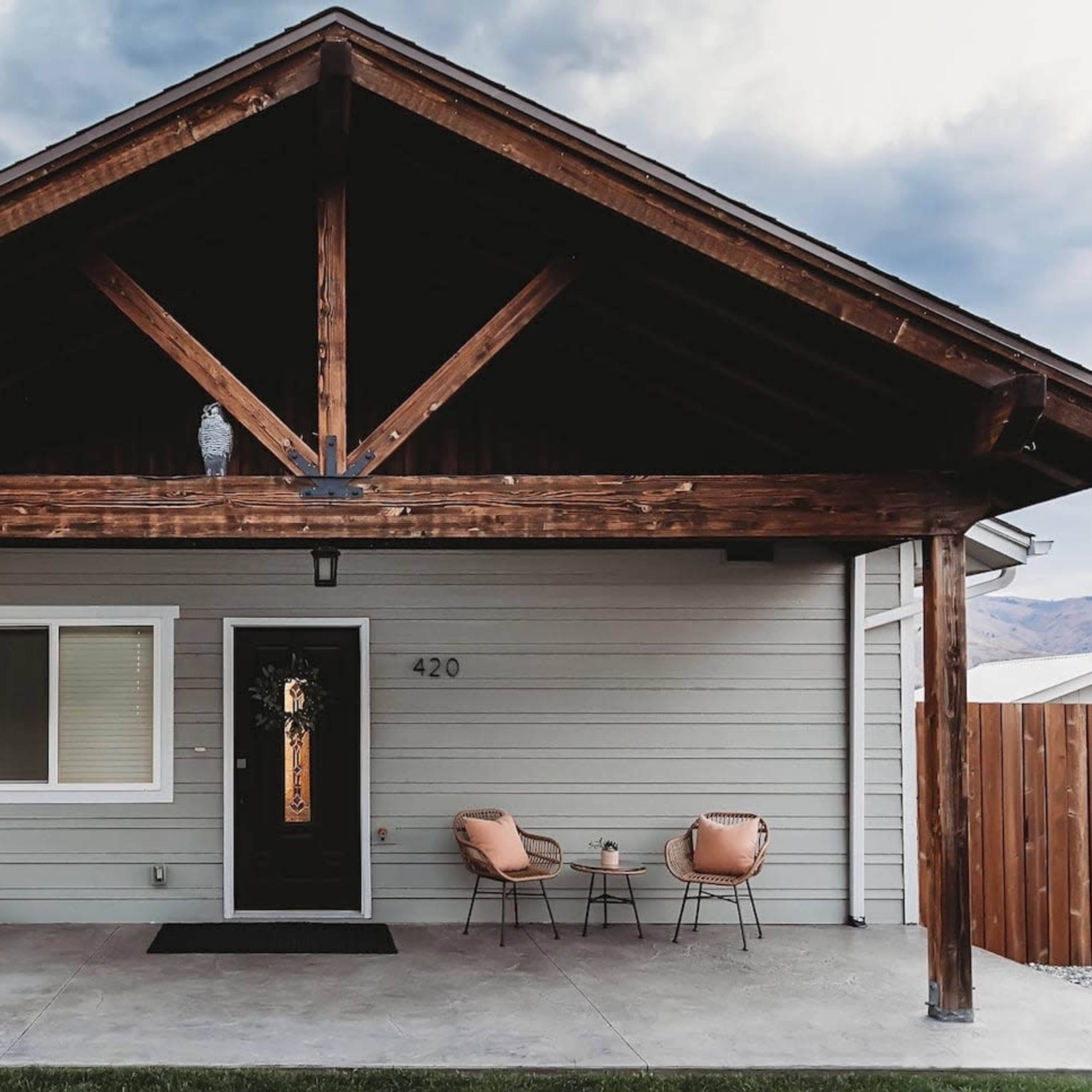 A modern home features a covered porch with two chairs and a swing under a wooden beam structure.