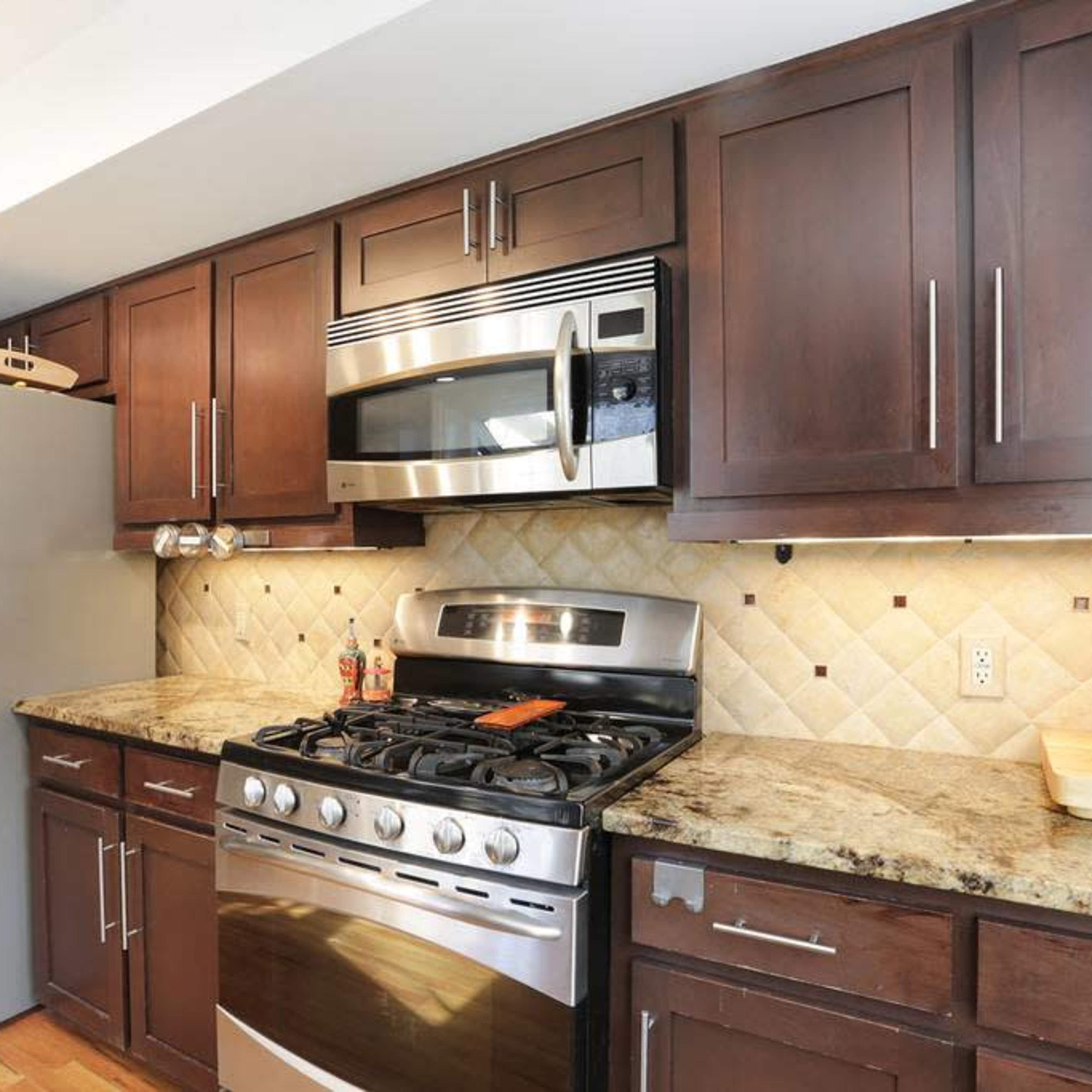 A kitchen with dark wood cabinetry, a stainless steel oven and microwave, and a granite countertop.
