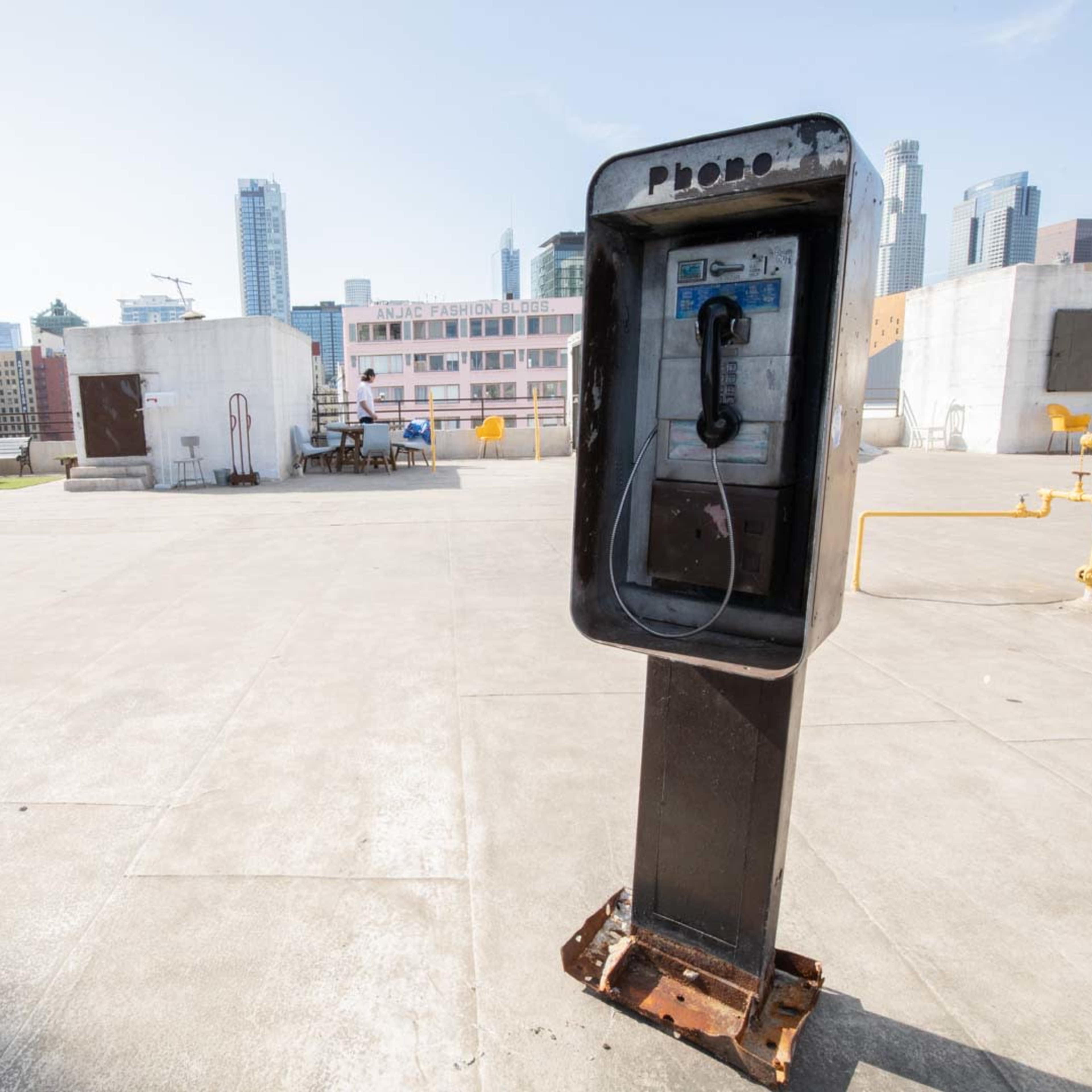 A payphone stands on a rooftop surrounded by city skyscrapers in the background.