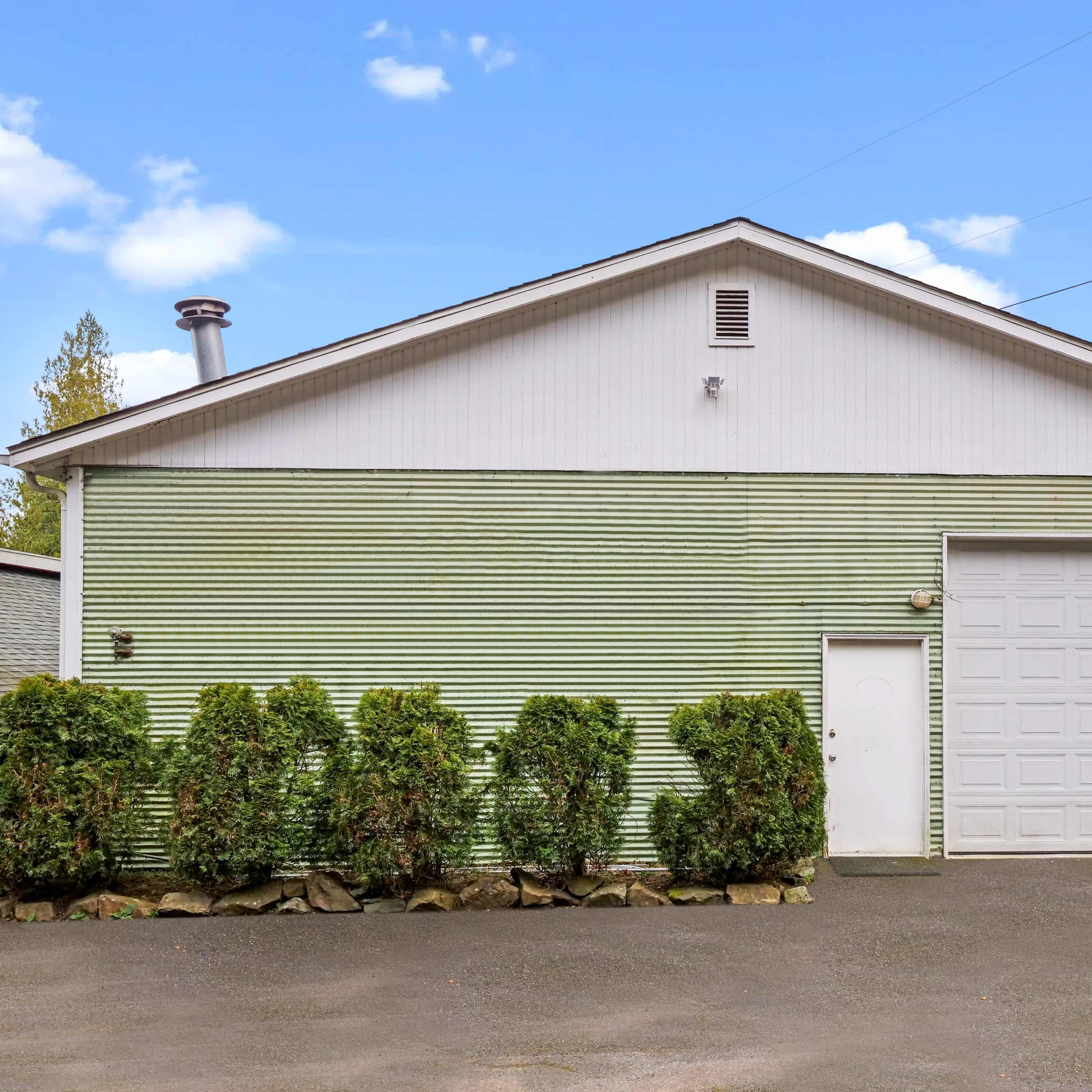 A one-story building with green horizontal siding and a single garage door faces a clear blue sky.