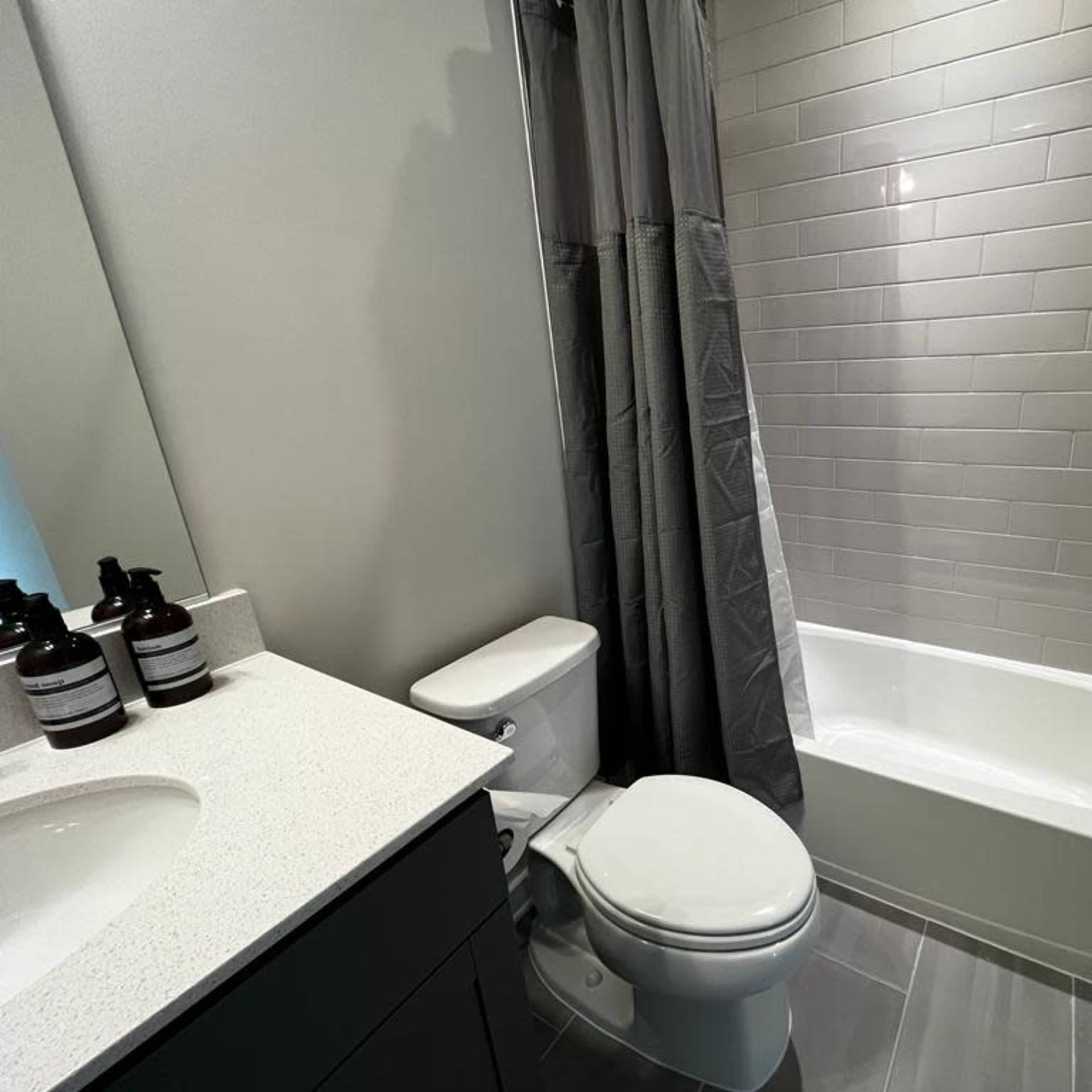 A modern bathroom featuring a bathtub with a shower curtain, a toilet, and a sink with a gray countertop.
