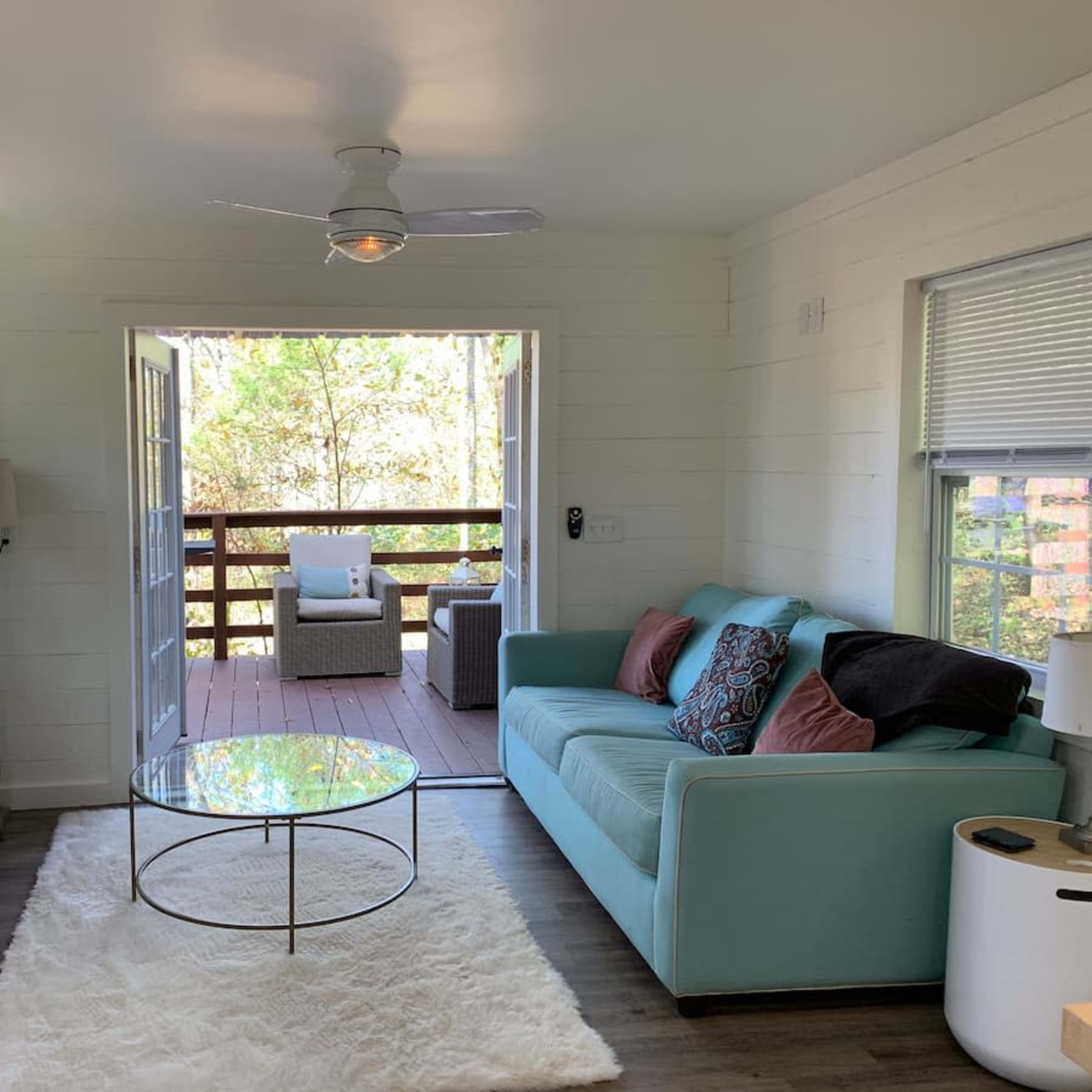 A cozy living room with a light blue couch, a round coffee table on a white rug, and sliding doors leading to a deck.