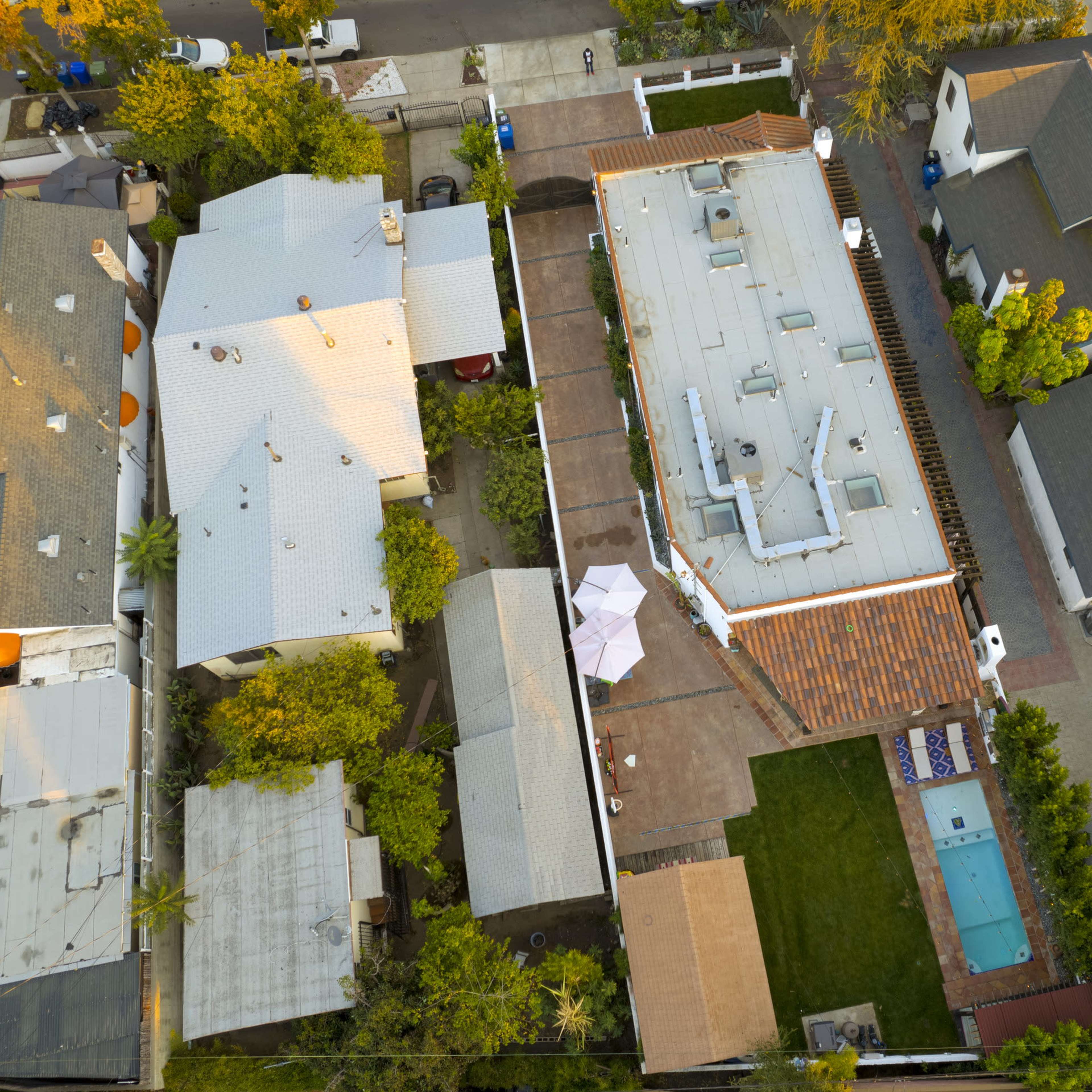 An aerial view of a residential neighborhood featuring several houses, a backyard with a swimming pool, and nearby outdoor seating areas.