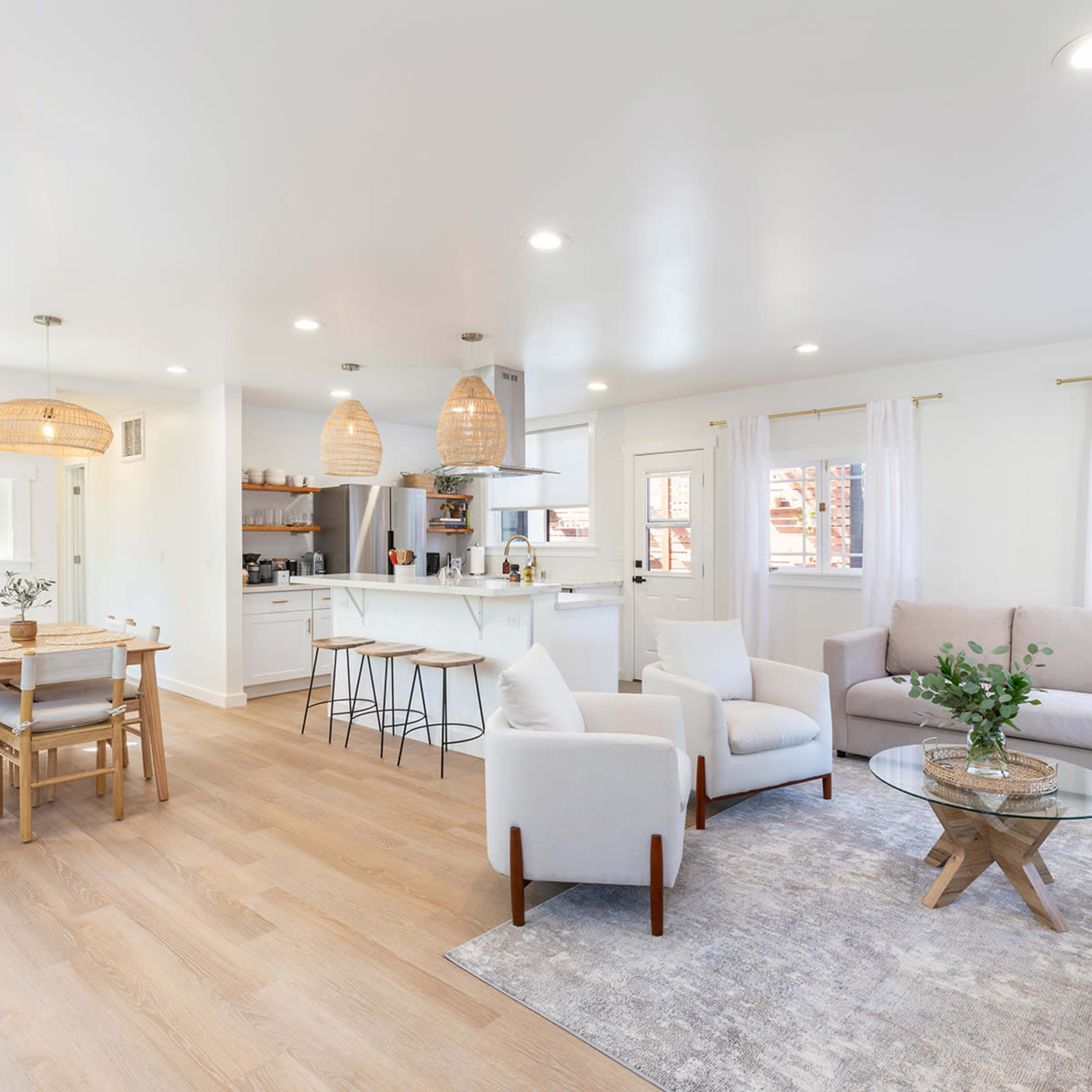 A modern, open-concept living space with a light-colored sofa, a dining area, and a kitchen visible in the background.