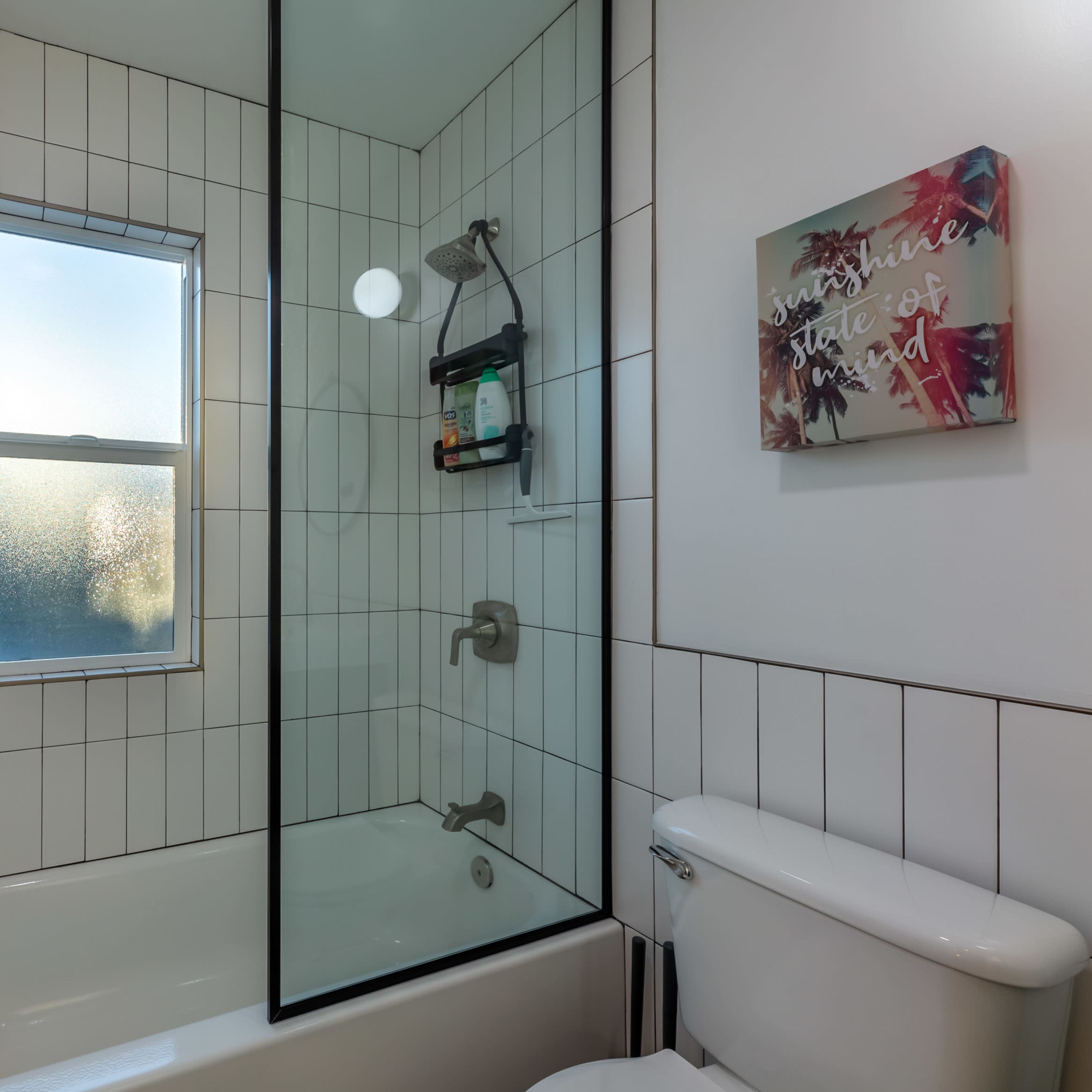 A modern bathroom featuring a glass shower enclosure, a bathtub, and a window allowing natural light.