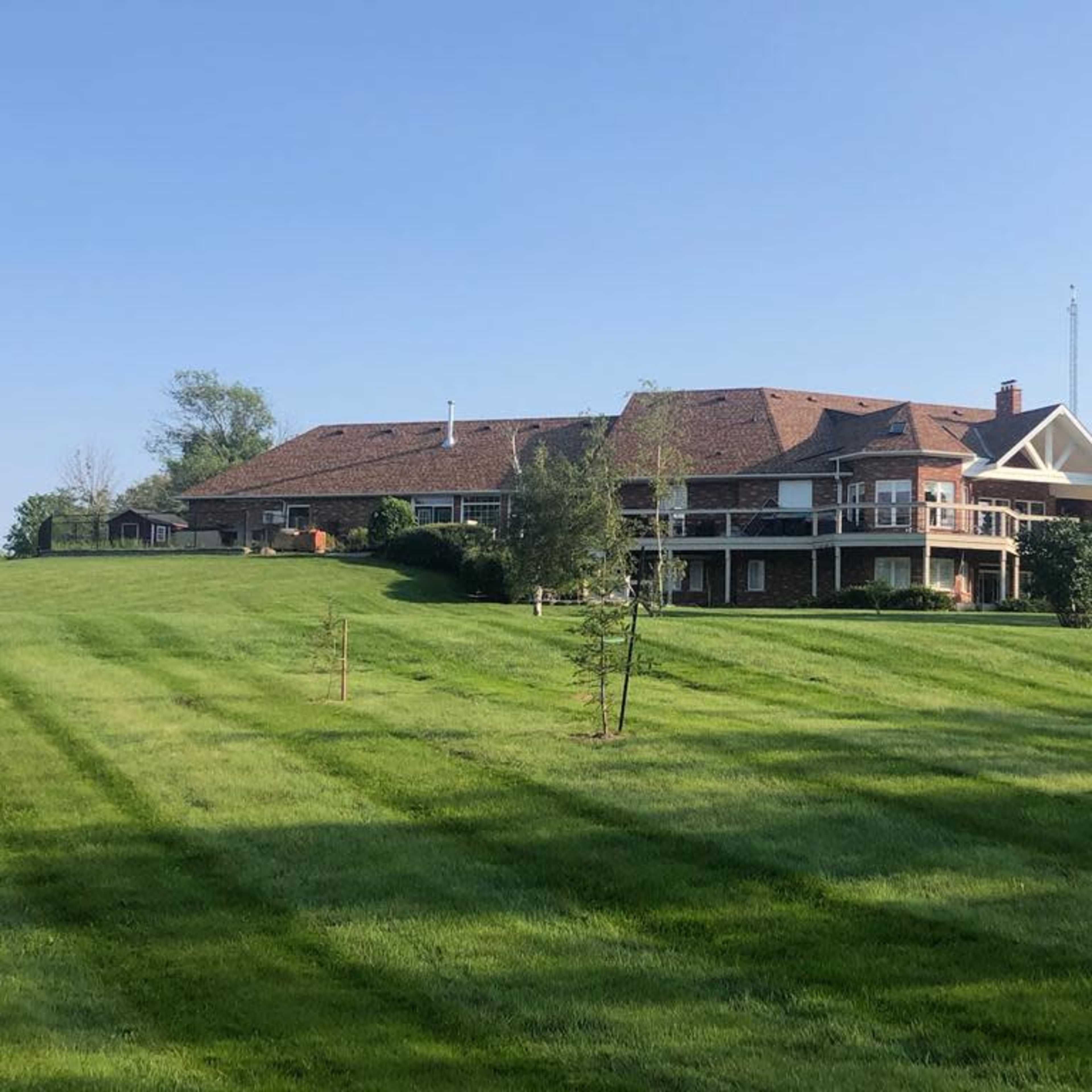 A large brick house with a sloped roof and multiple balconies is situated on a lush green hillside.