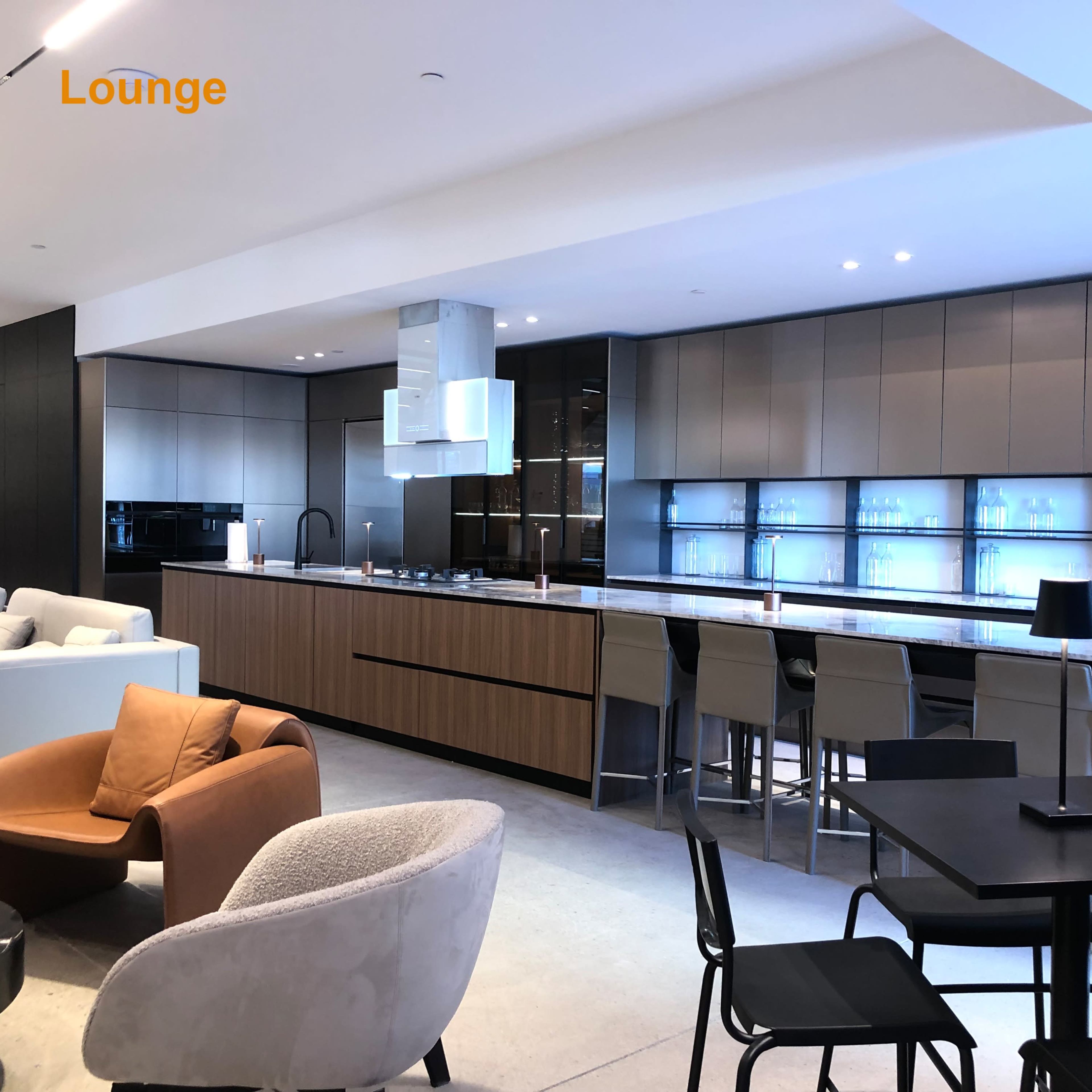 A modern kitchen and lounge area features a long countertop, bar seating, and various seating options in a spacious layout.