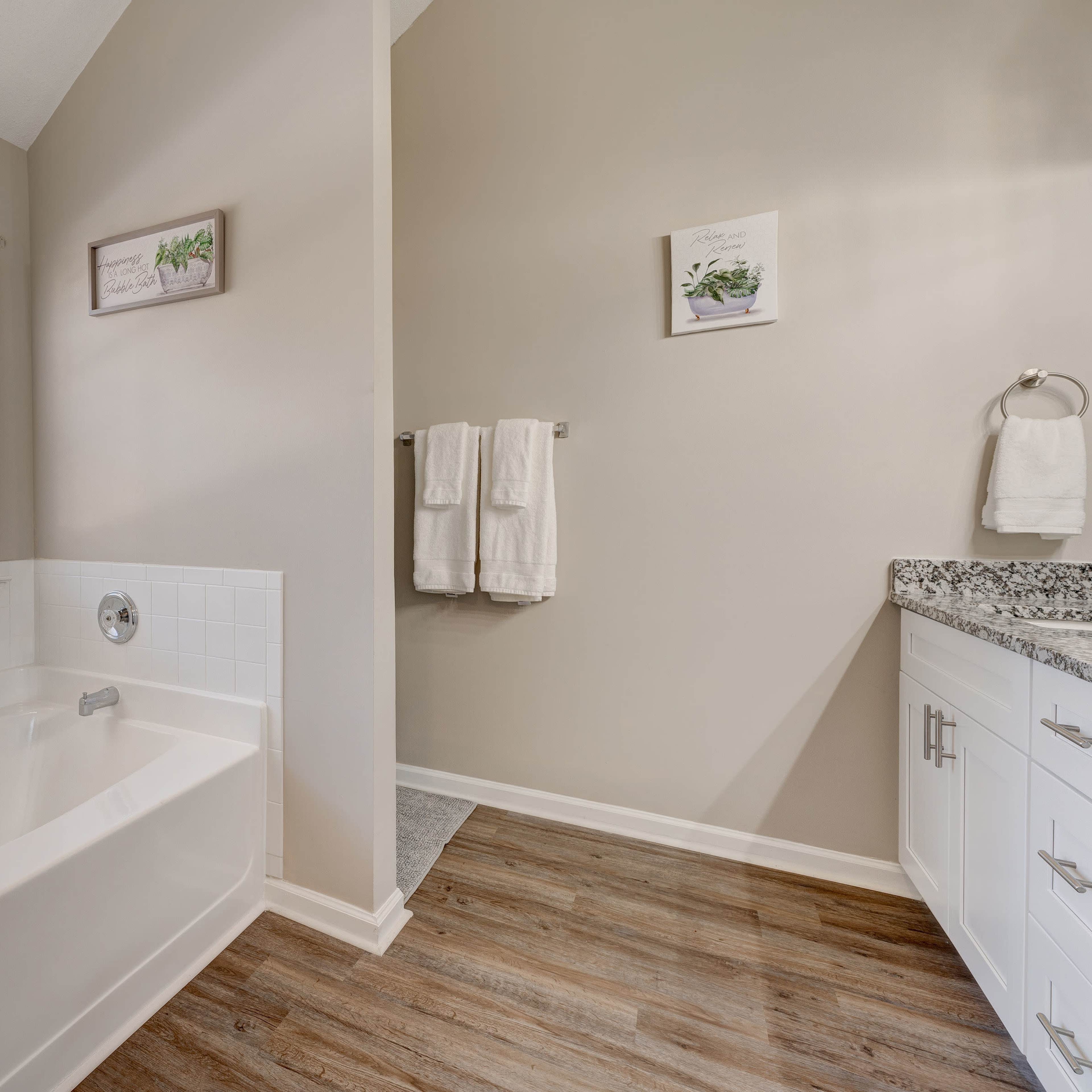 A bathroom with a white bathtub beside a window, a sink area with a granite countertop, and a towel rack on the wall.