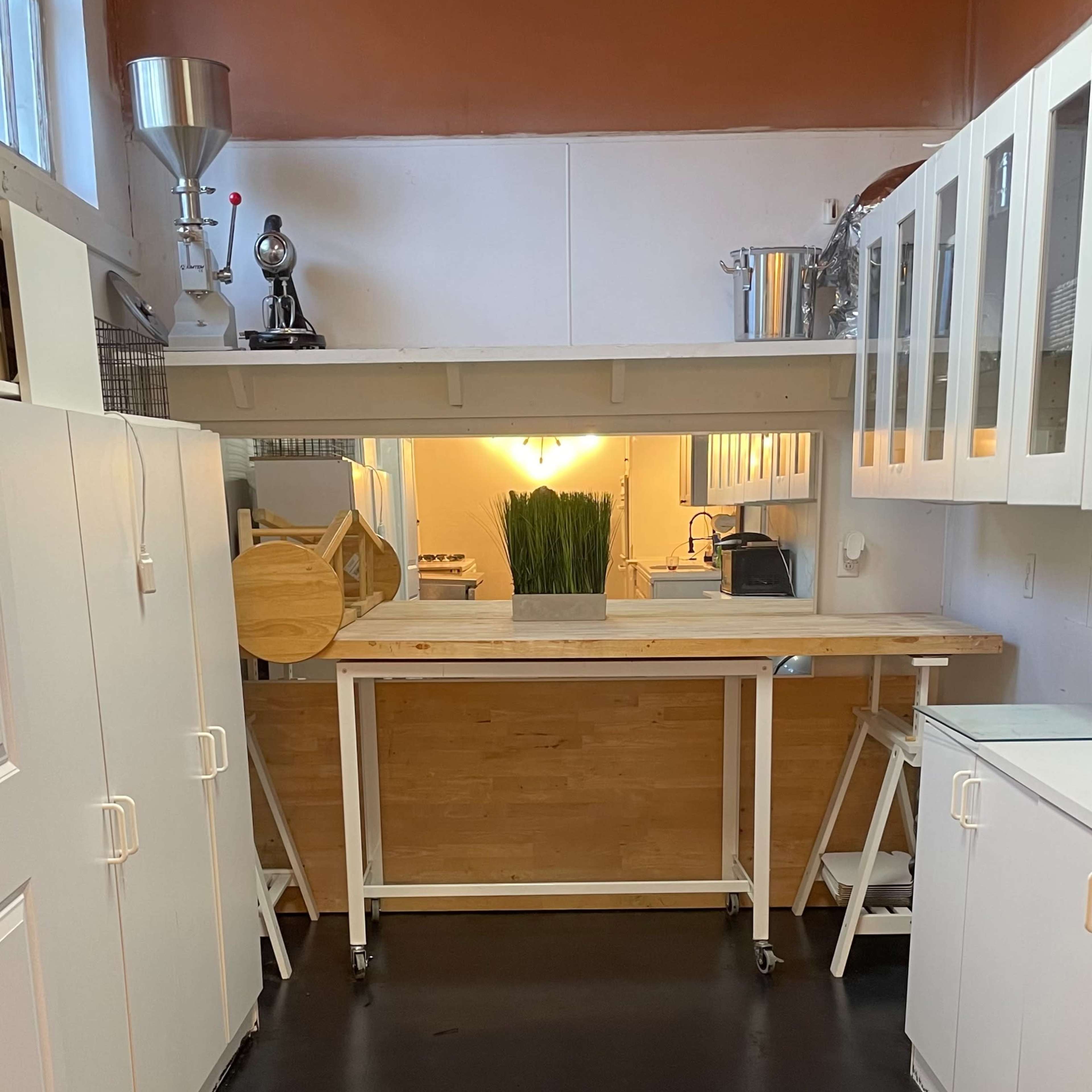 A modern kitchen featuring white cabinets, a wooden countertop, and a lit area in the background with greenery.