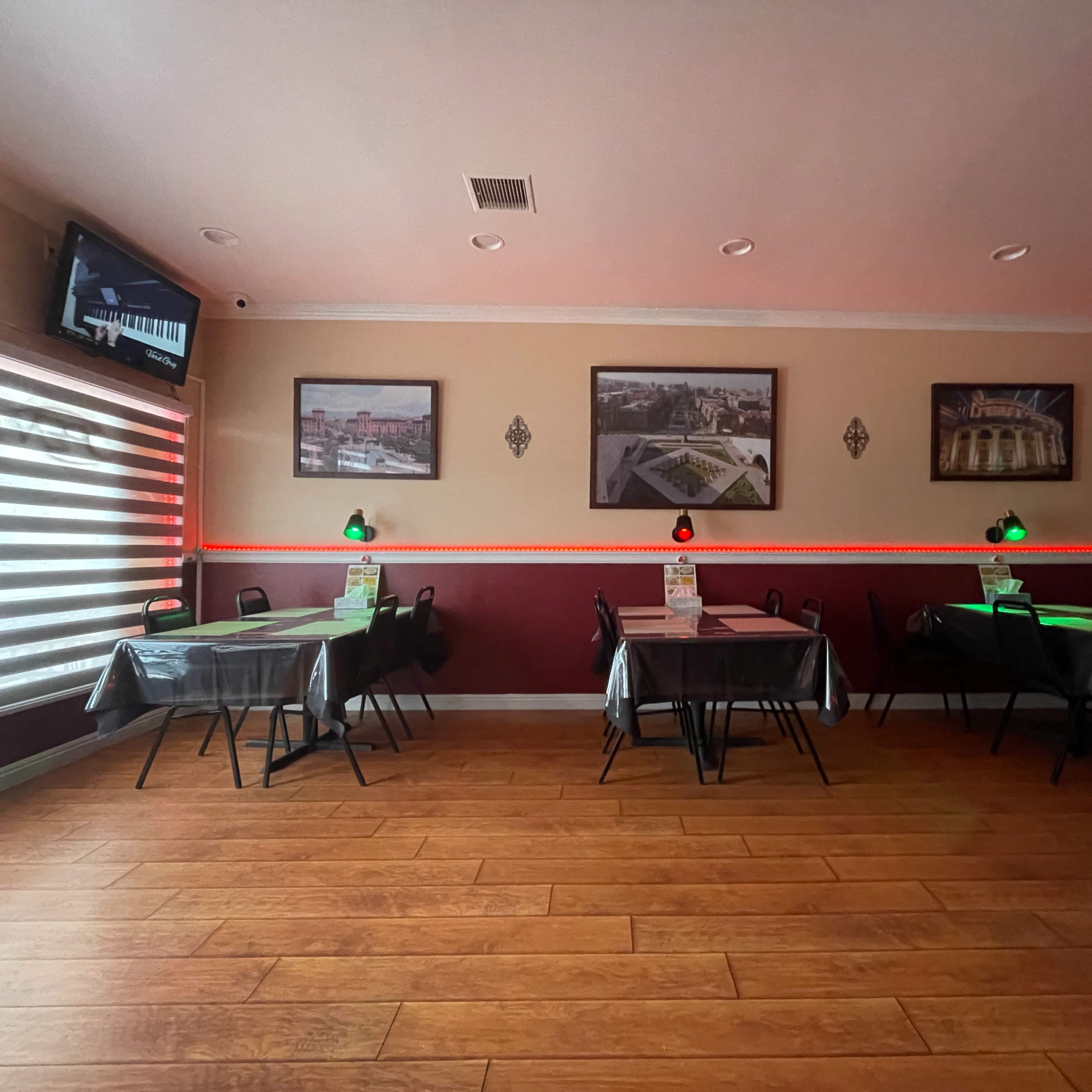 A dining area of a restaurant with several tables, illuminated by green lamps, and decorated with framed photos on the walls.