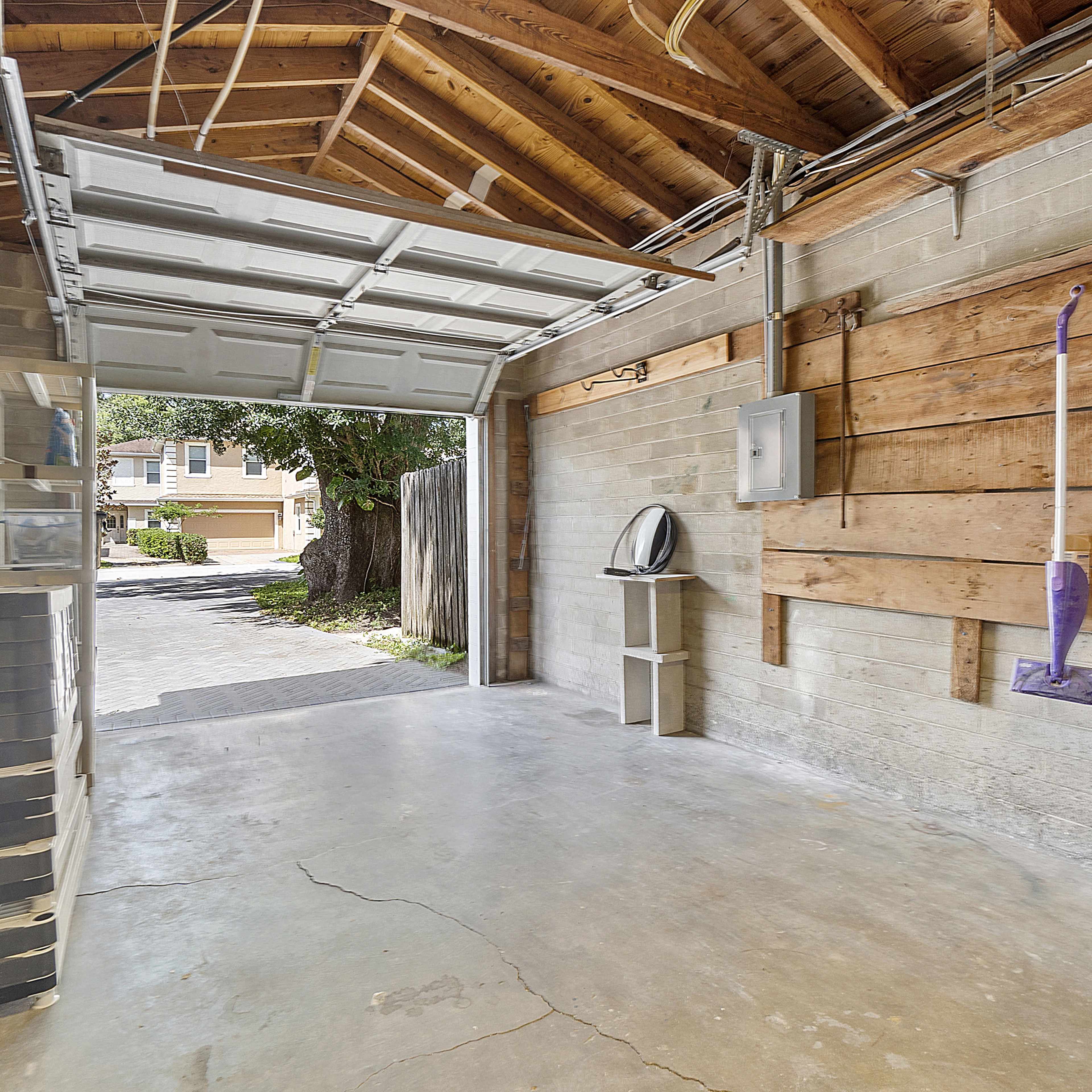 A garage with an open door, revealing a concrete floor, walls partially lined with wood paneling, and a few items stored against the walls.