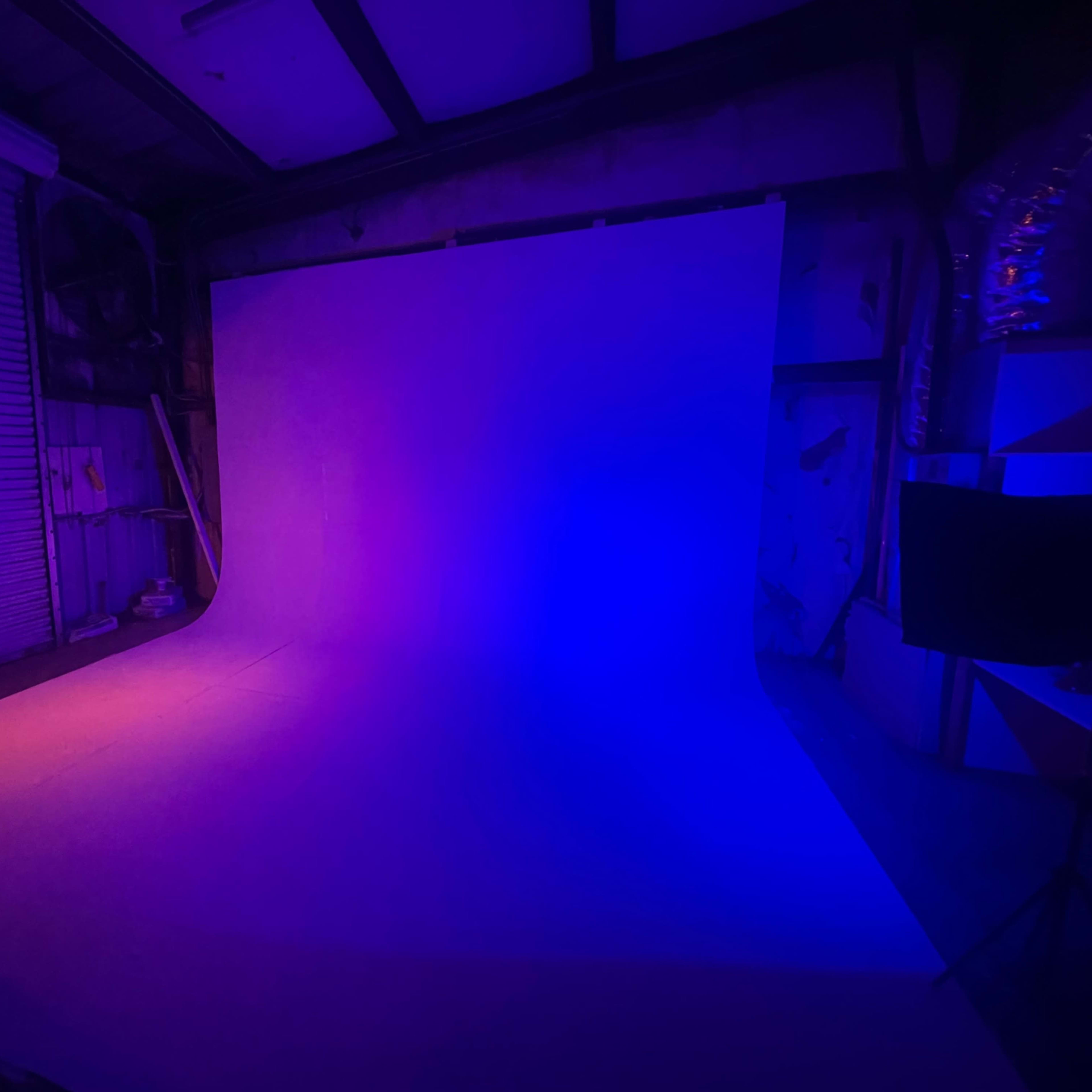 A photography studio with a curved backdrop illuminated in purple and orange light.