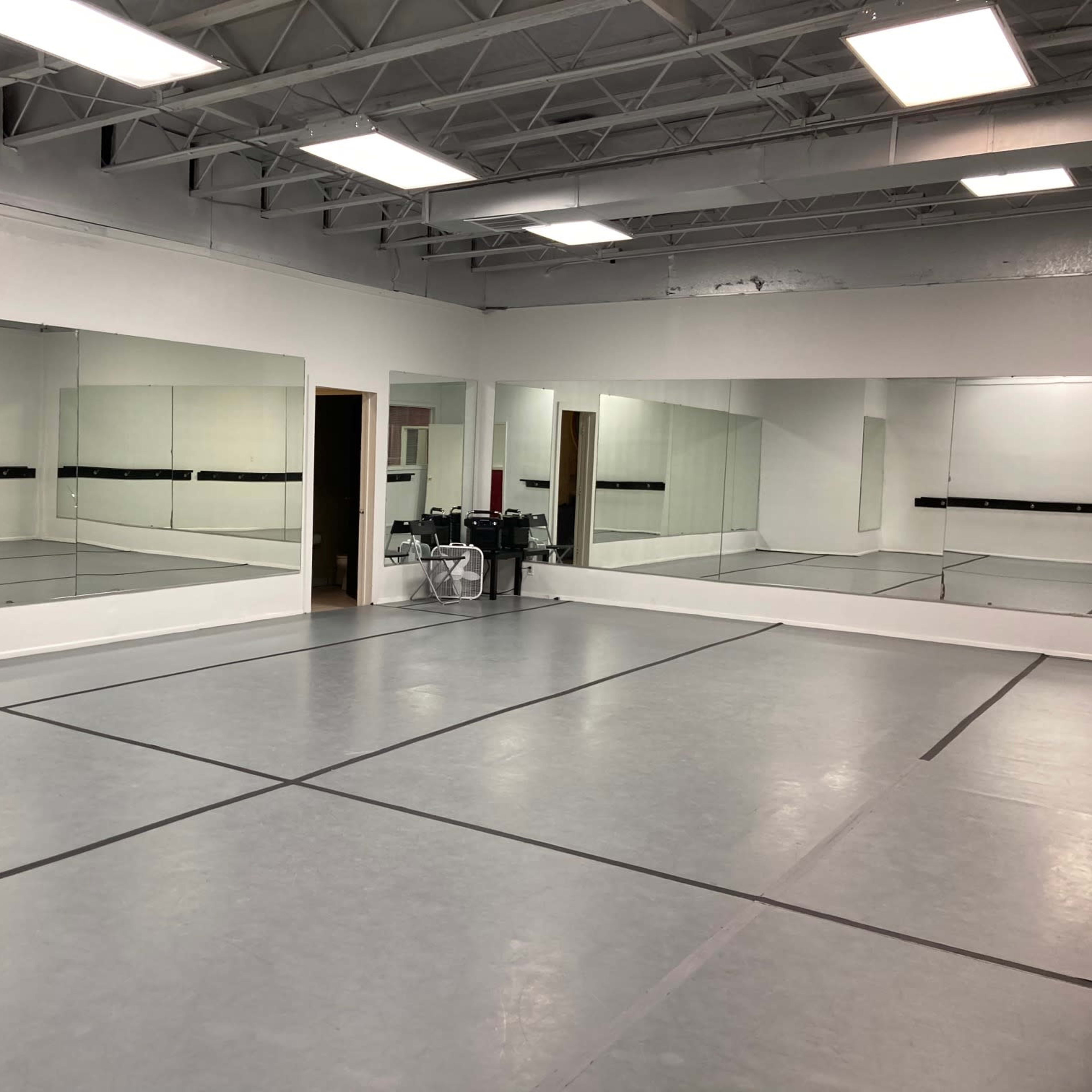 A spacious dance studio with mirrored walls and a gray flooring marked by black lines.