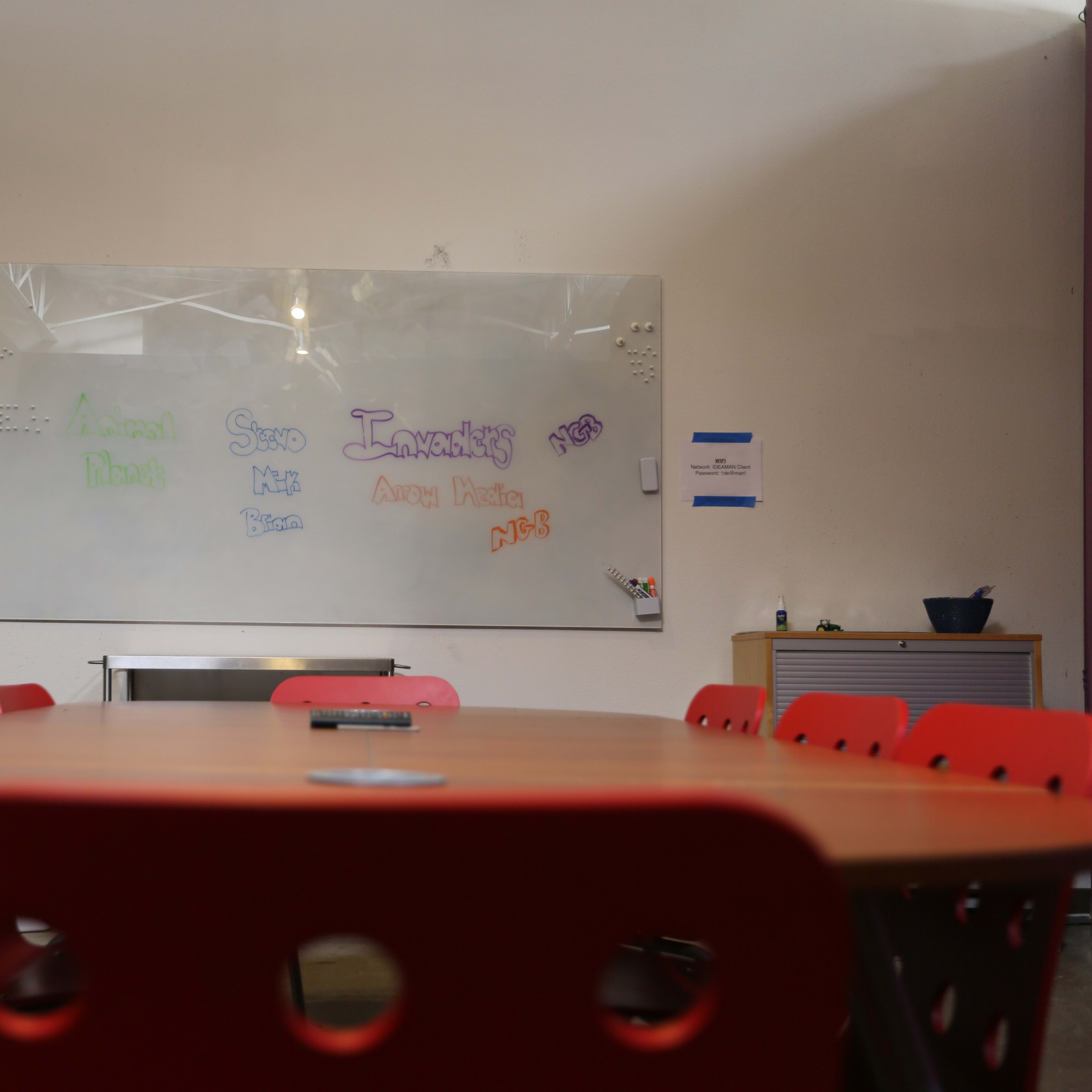 A conference room with a large table surrounded by red chairs and a whiteboard featuring colorful text on one wall.