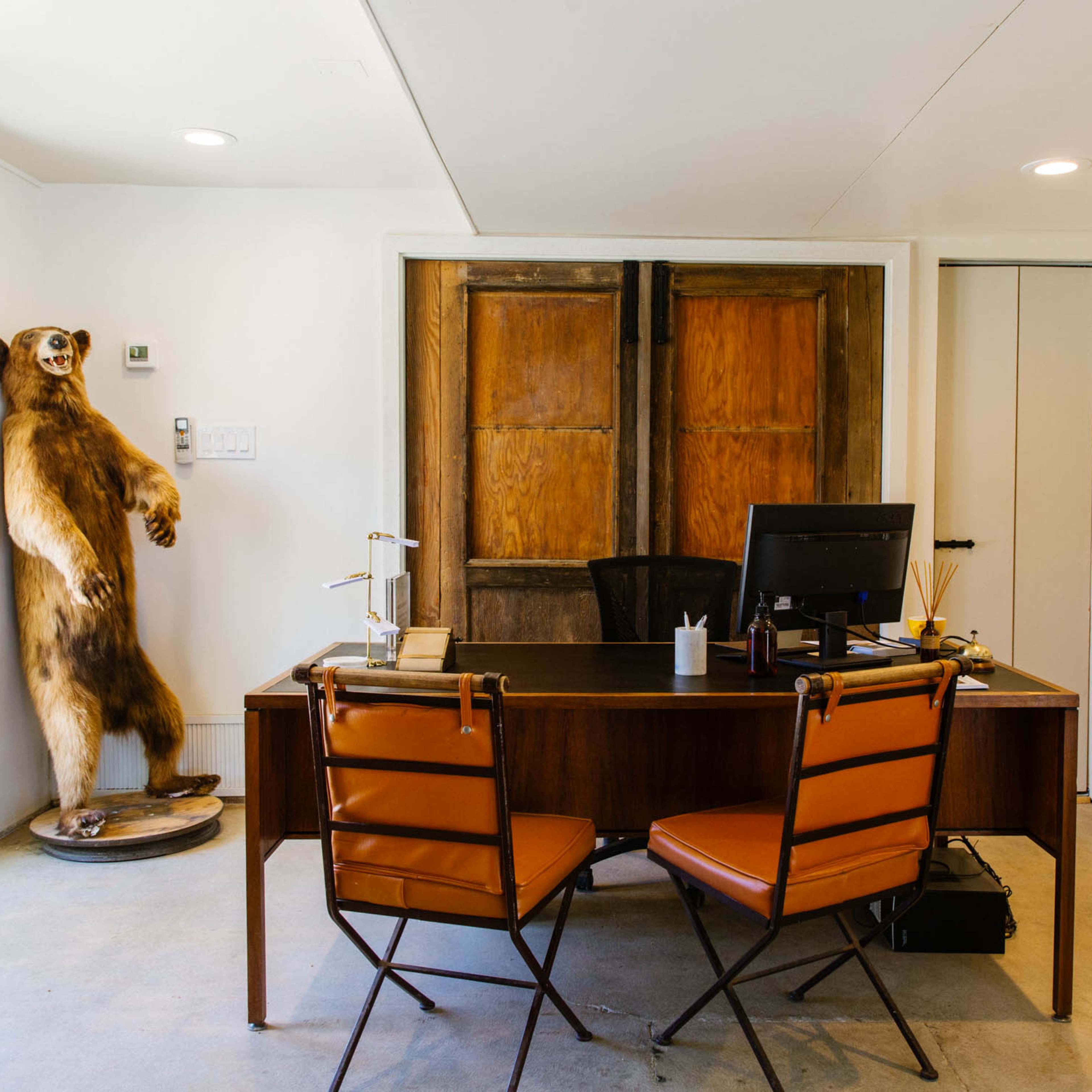 A small office with a desk, a computer, and a mounted bear standing next to a set of wooden double doors.