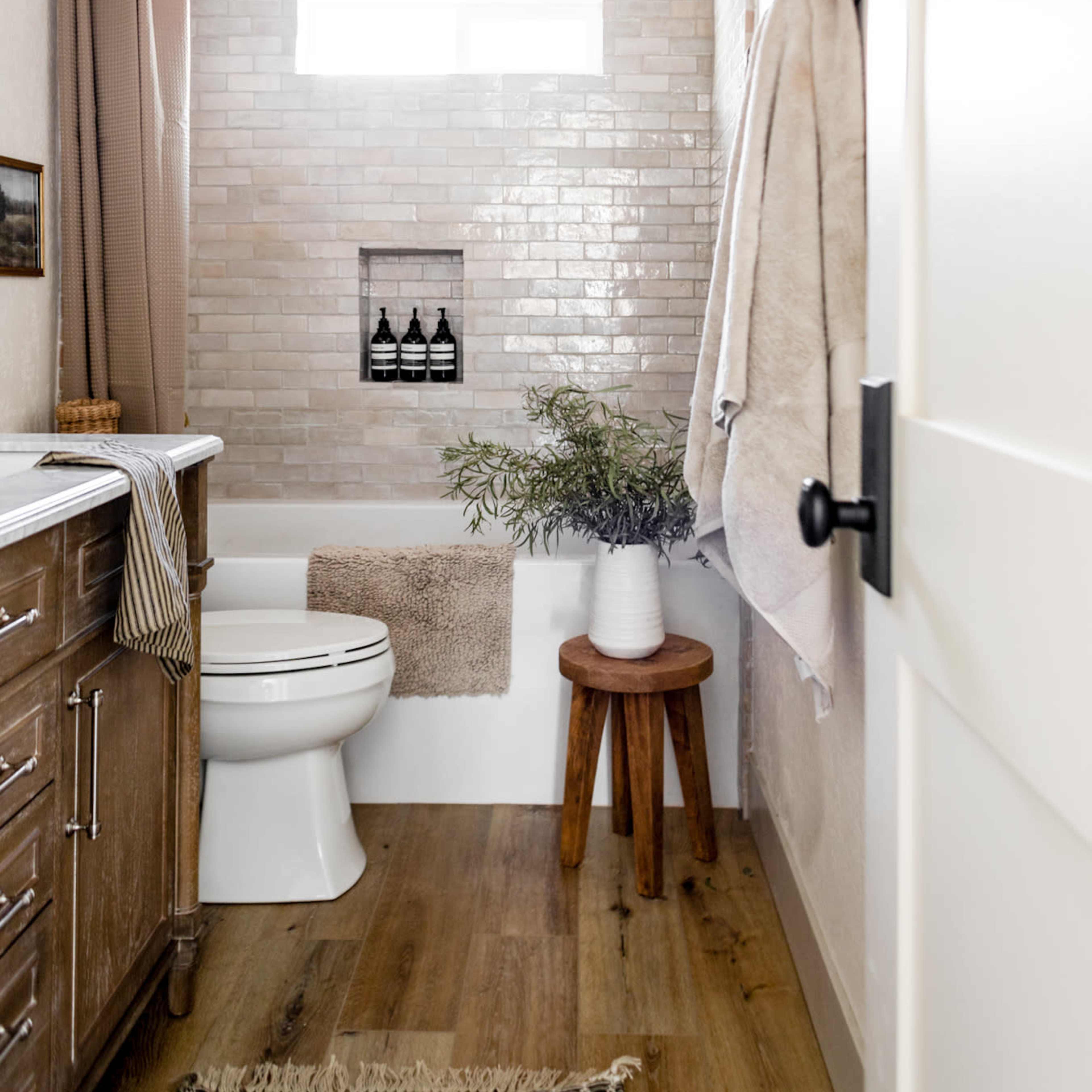 The bathroom features a shower with tiled walls, a wooden countertop with storage, and a small window above the tub.