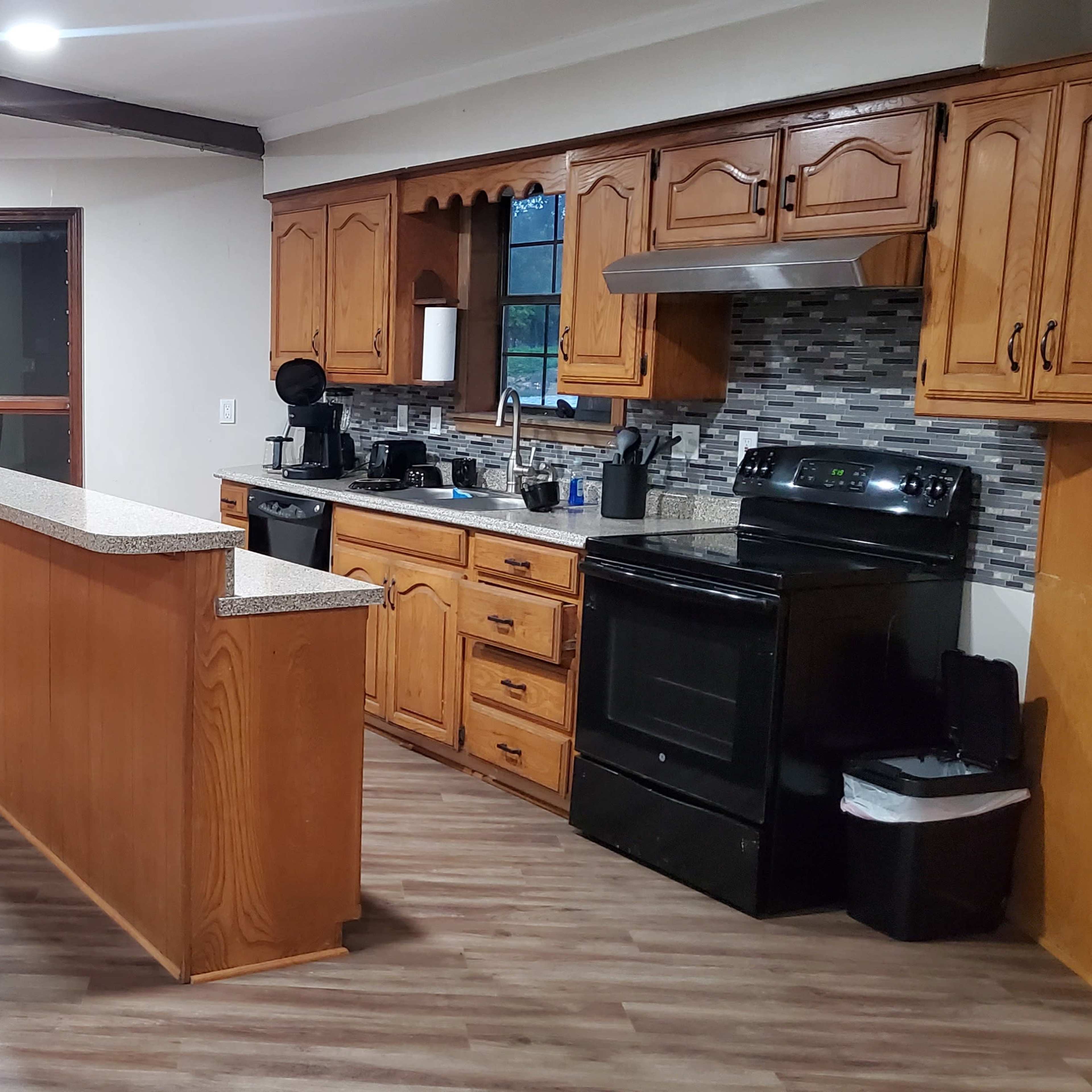 A kitchen area features wooden cabinets, a countertop island, and a dining table with chairs, adjacent to a window with a view.