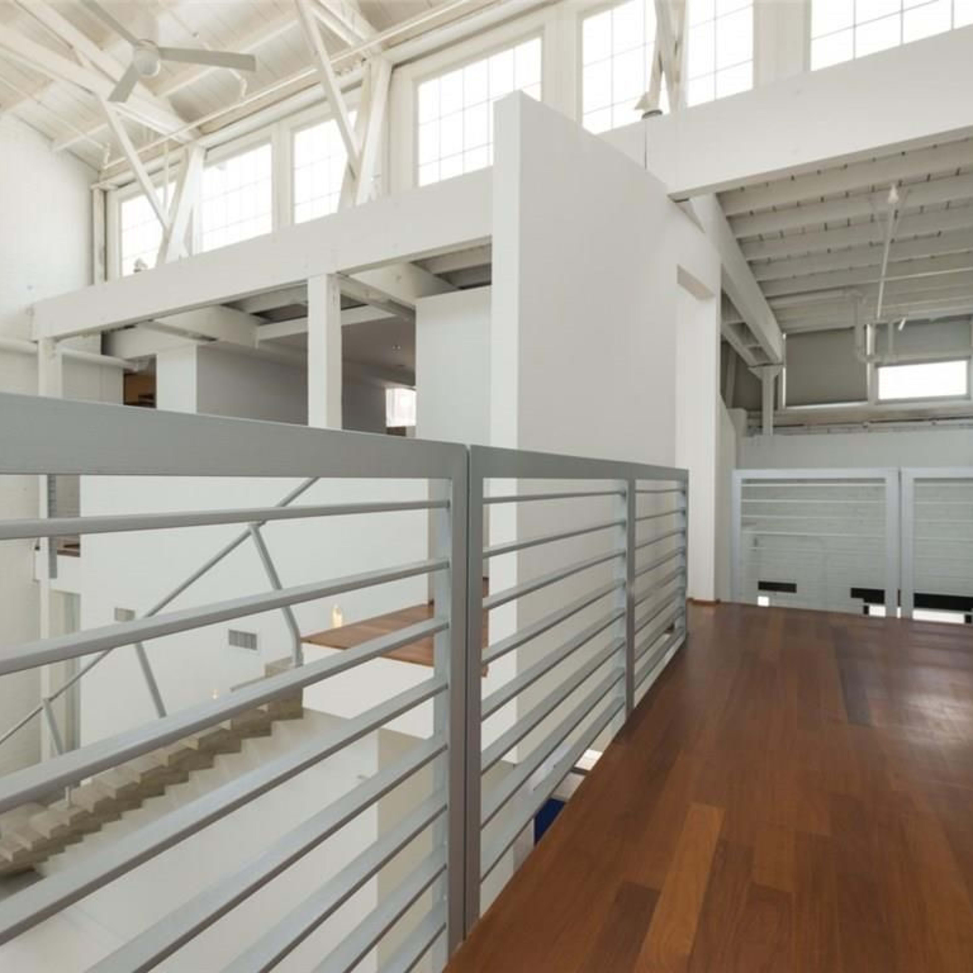 A modern interior space with a wooden balcony overlooking a staircase and open floor plan beneath.