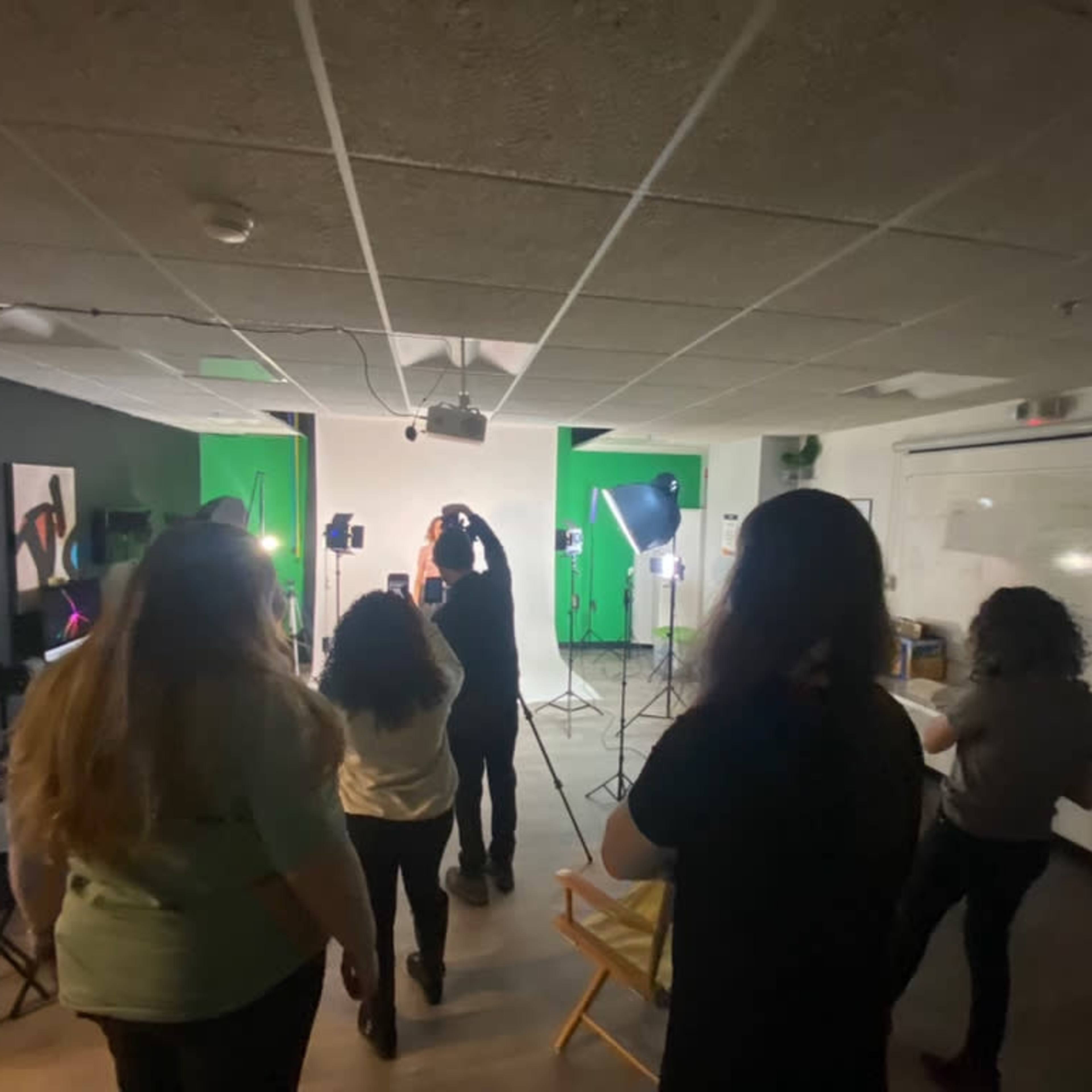 A group of people is standing in a studio with green screens and lighting equipment set up for a photoshoot.