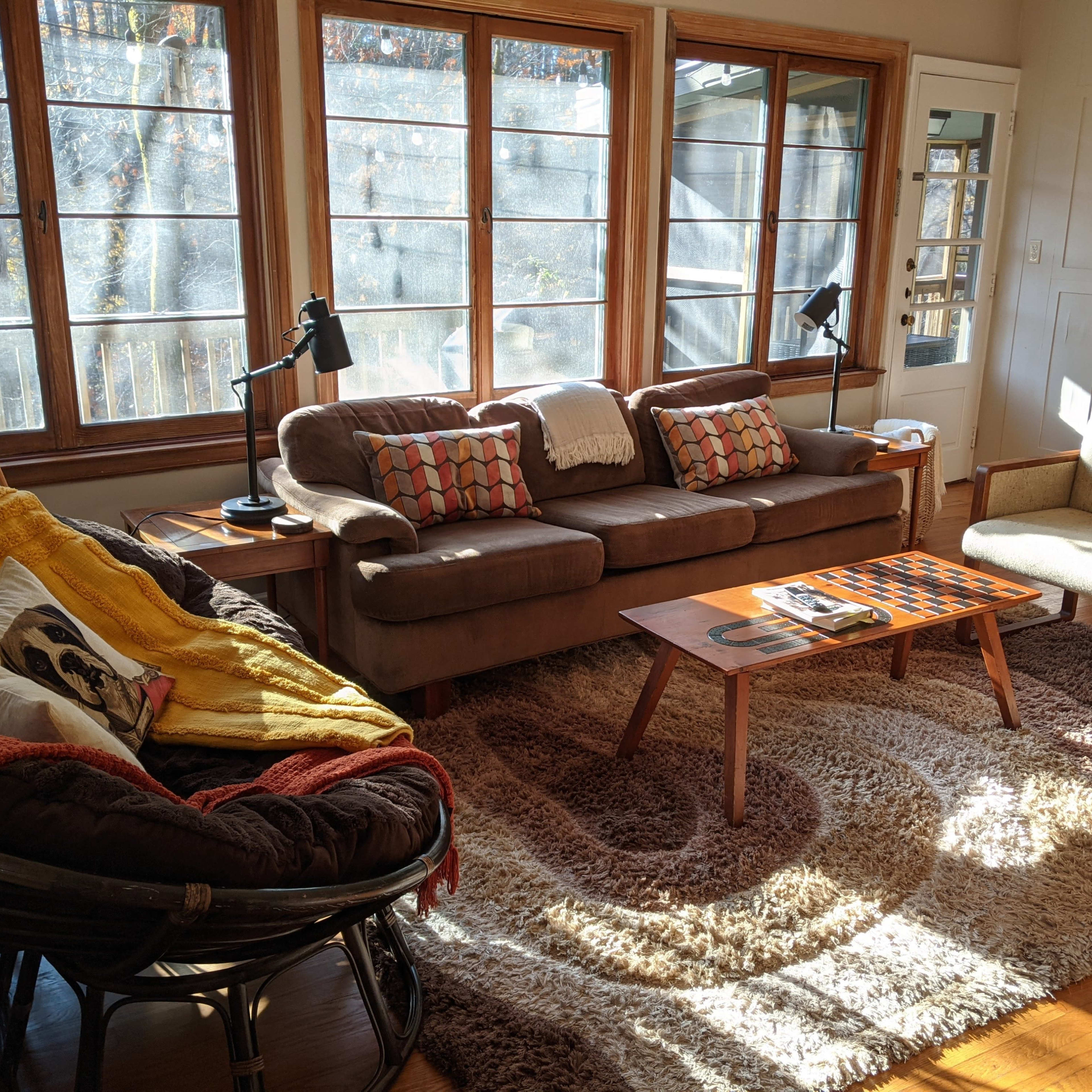 The living room features a sofa, an armchair, a coffee table with a checkerboard, and large windows allowing natural light.